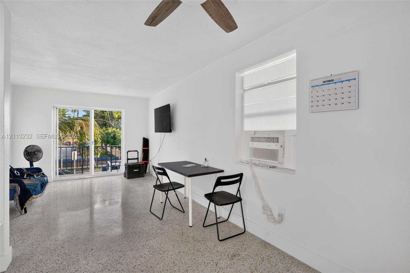 Polished terrazzo flooring, sliding glass door access to a balcony, and a ceiling fan with wood-finish blades