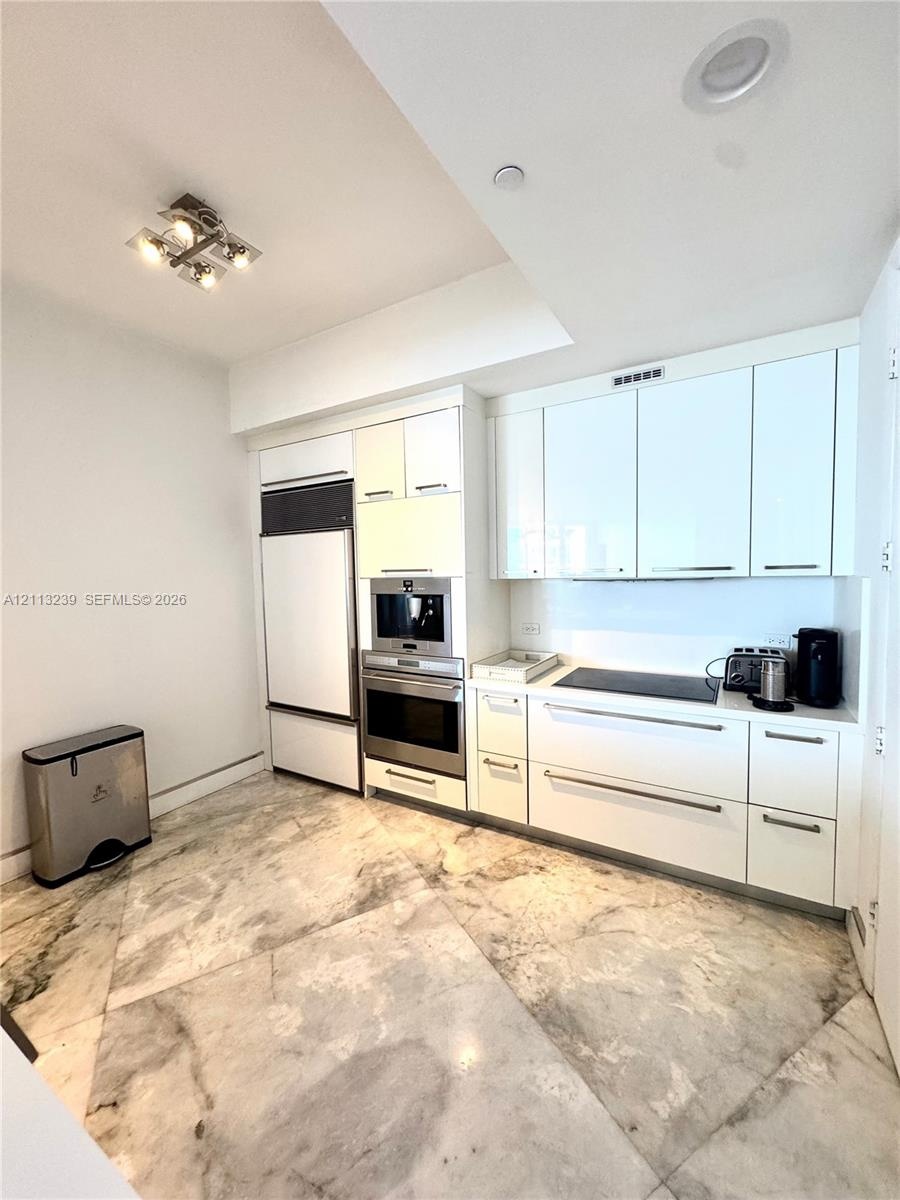Sleek kitchen featuring high-gloss cabinetry, integrated stainless steel appliances, a built-in wall oven, a flat-surface cooktop, and large-format ti