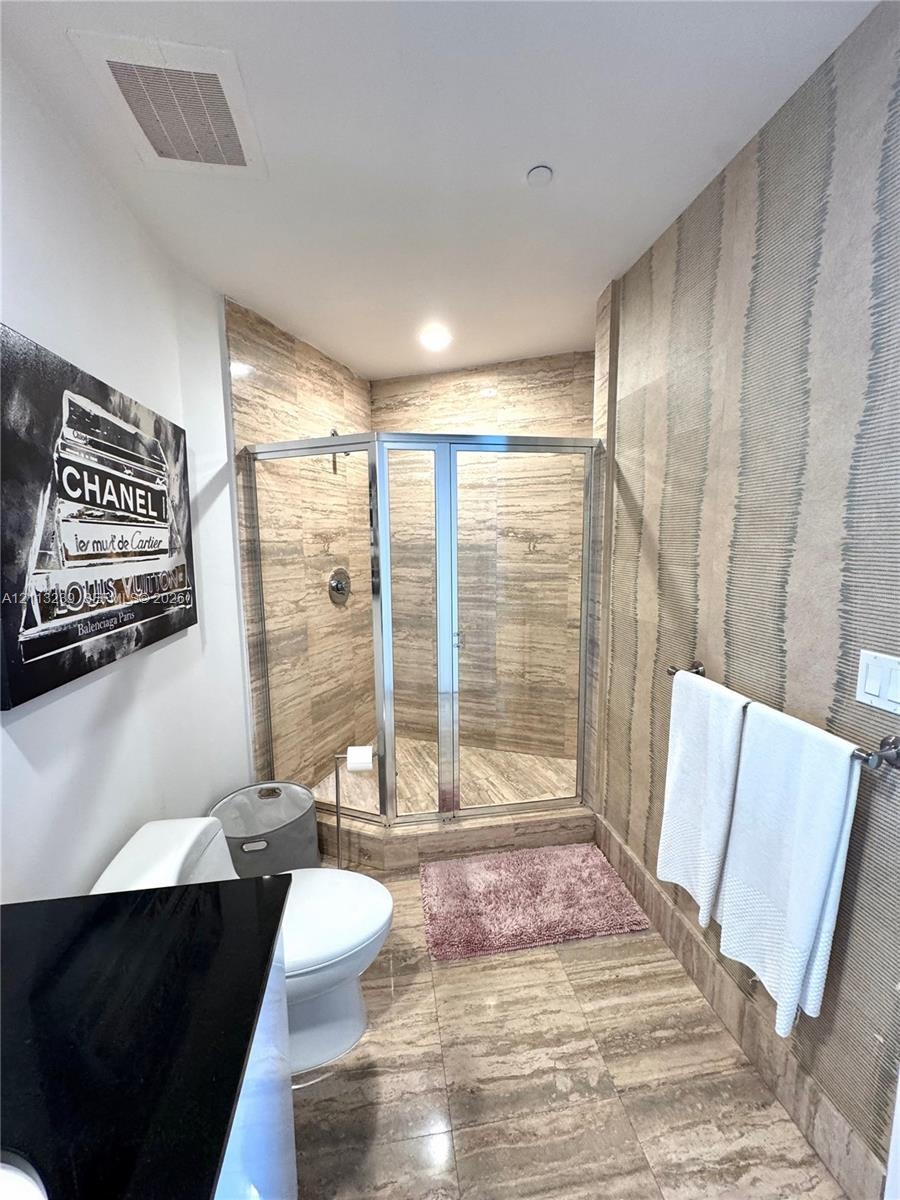 Bathroom featuring a corner glass-enclosed shower, stone tile flooring, stone-tiled shower walls, wall-mounted metallic towel bar, and textured wall t