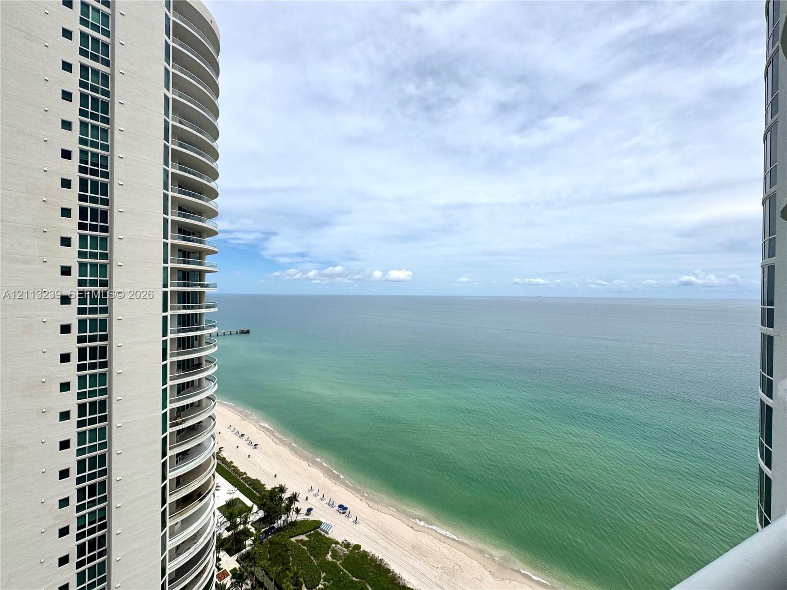 High-rise balconies with glass railings overlooking a coastal shoreline and ocean expanse