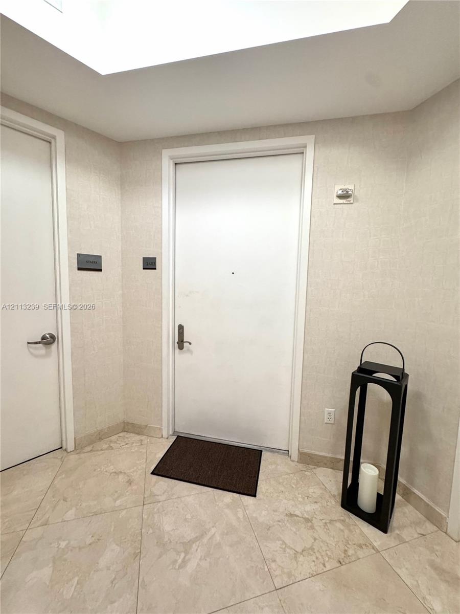 Entryway featuring neutral-toned tile flooring, textured wall coverings, and a recessed ceiling panel
