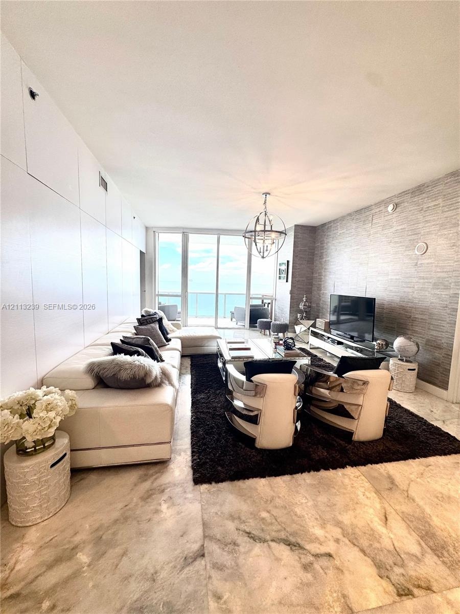Living area featuring floor-to-ceiling glass paneling, stone tile flooring, a textured feature wall, and a contemporary spherical pendant light fixtur