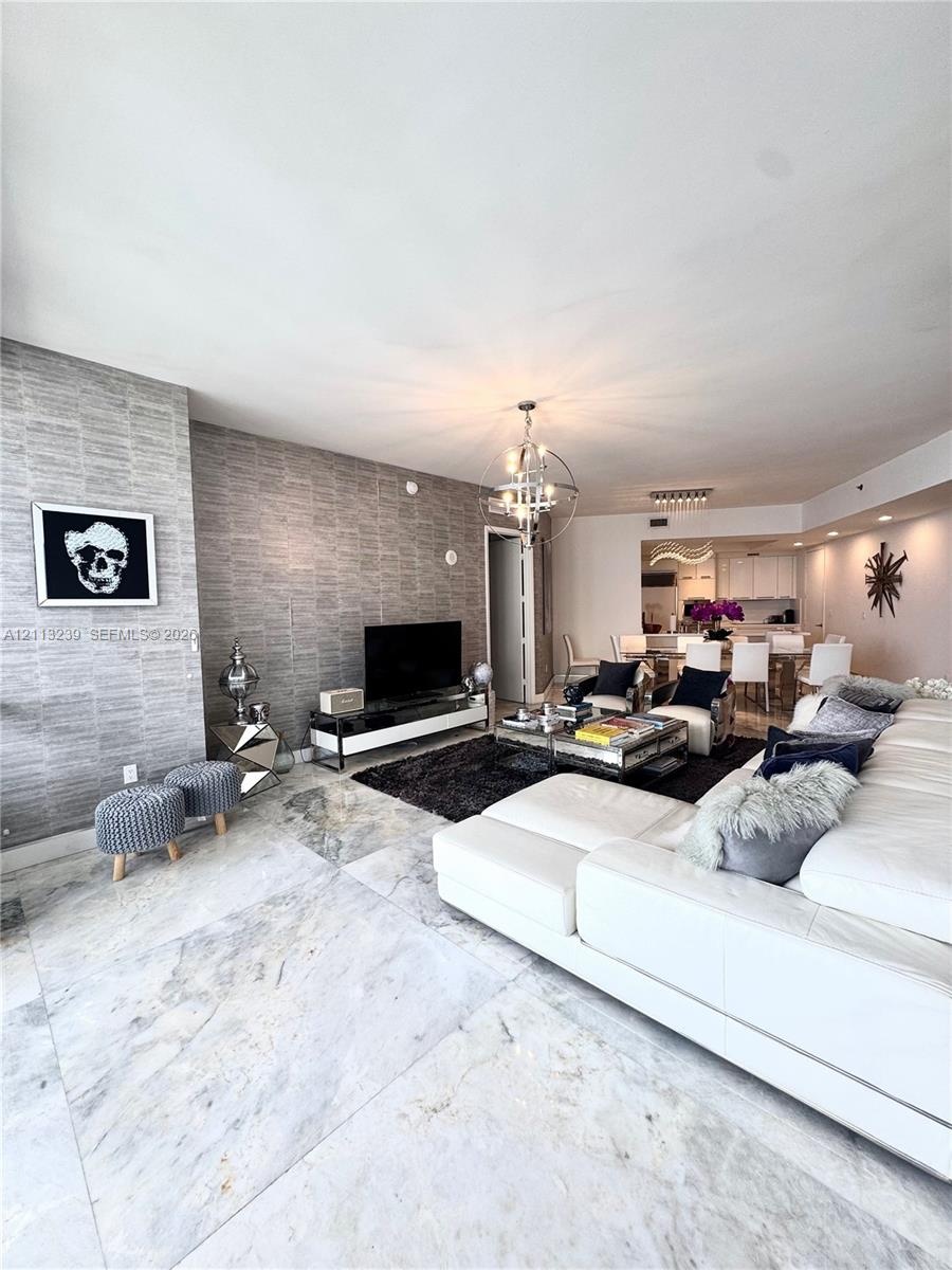 Large-format tile flooring, textured stone-finish accent wall, spherical orb-style chandelier, and recessed ceiling lighting