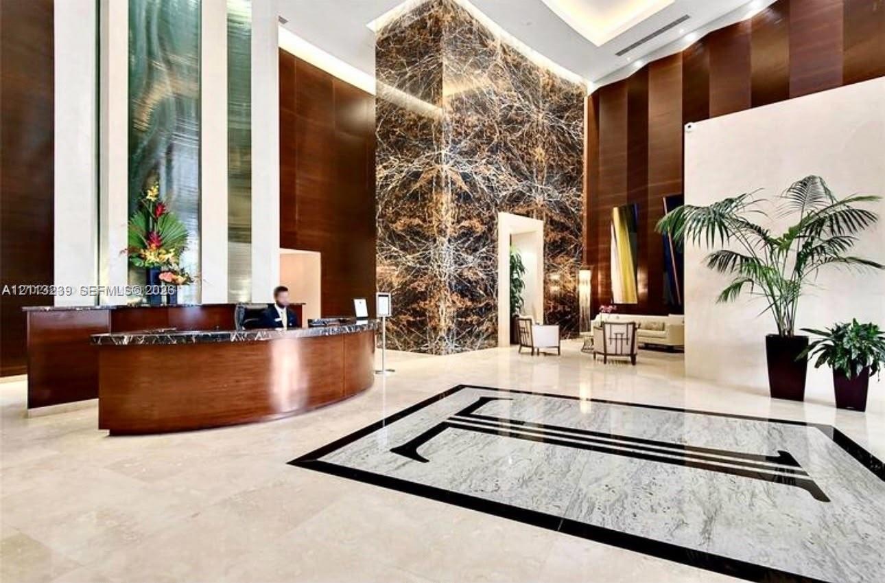 Grand lobby entrance featuring high-contrast stone flooring, a prominent full-height natural stone feature pillar, recessed cove lighting, and curved 