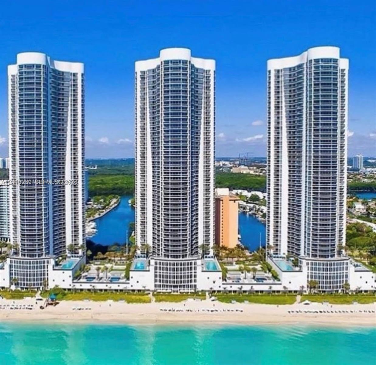 High-rise residential towers featuring glass-paneled balconies, exterior swimming pools, direct beachfront access, and water-front placement