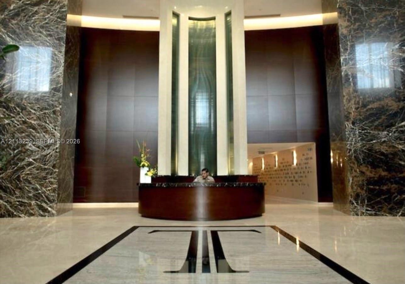 Grand entrance featuring floor-to-ceiling stone wall cladding, polished stone flooring with geometric inlay, and a built-in concierge desk