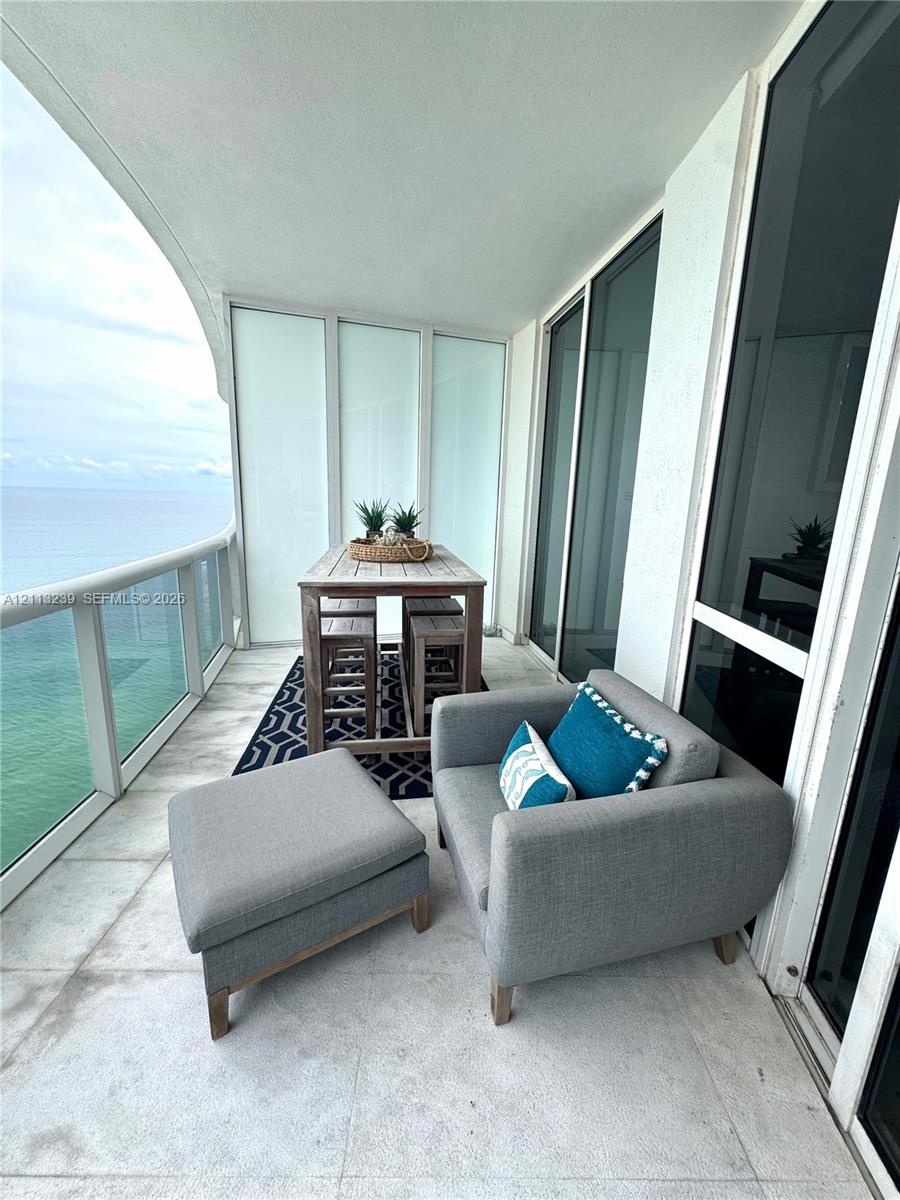 Covered balcony featuring large-format stone tile flooring, a glass panel railing, and expansive floor-to-ceiling glass sliding doors