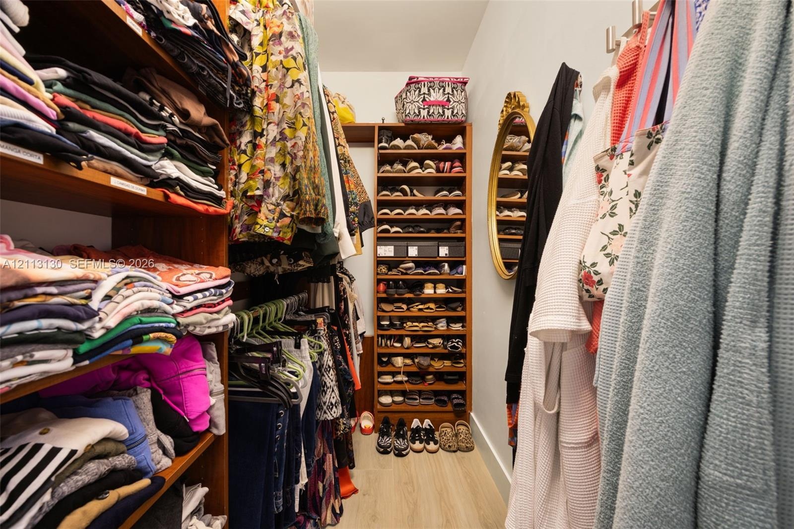 Walk-in closet featuring custom wood-finish shelving units, integrated floor-to-ceiling shoe storage, and wall-mounted garment hooks