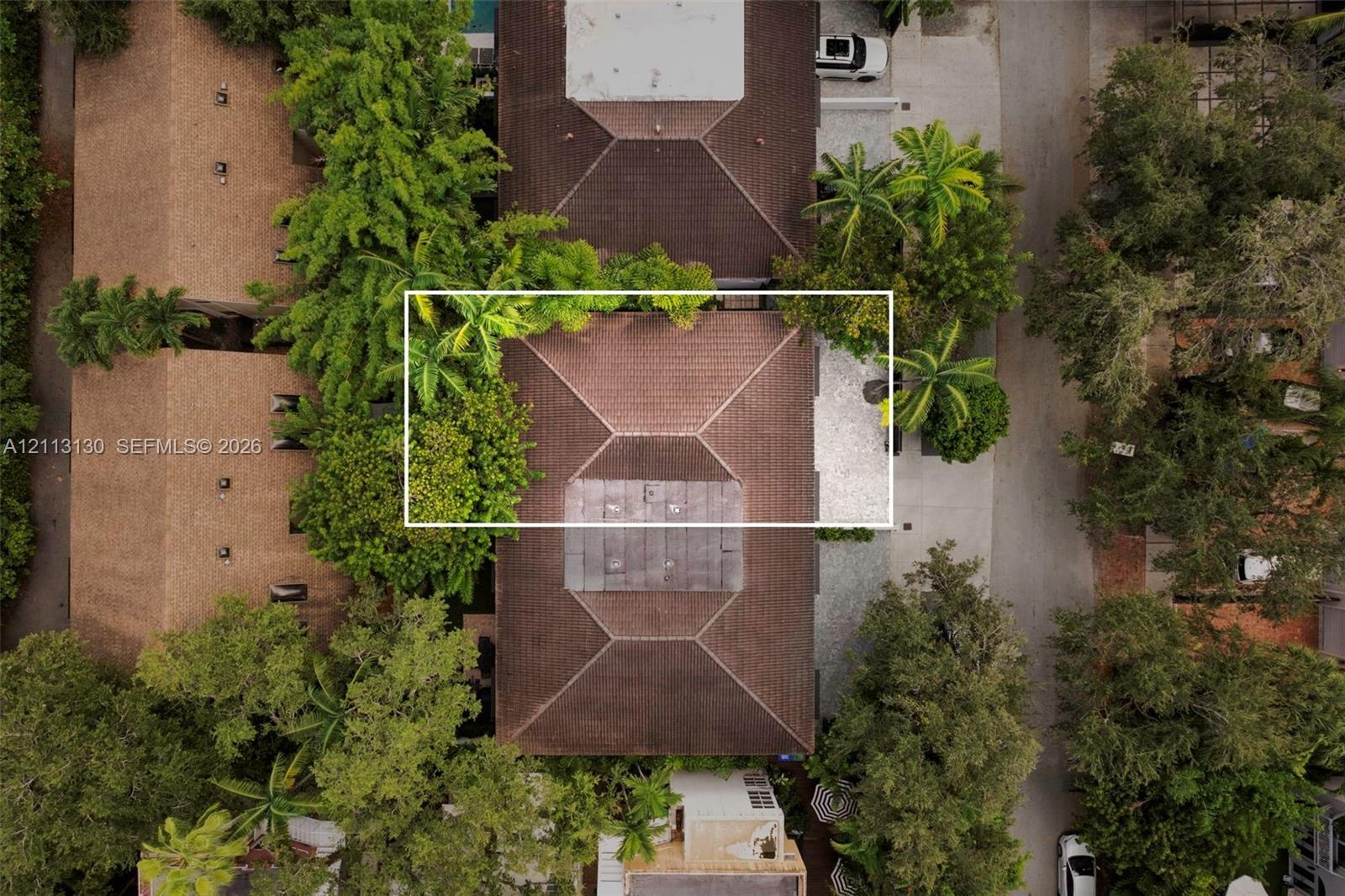 Aerial perspective of a multi-sectioned hip roof featuring dark shingle tiling, integrated solar panels, and surrounding mature landscaping