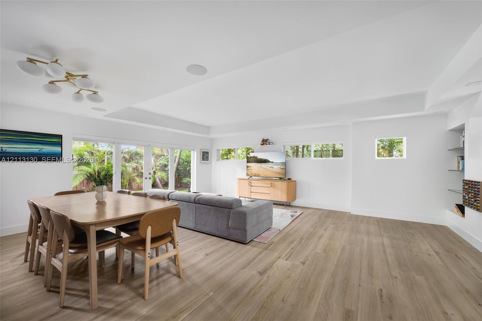 Open-concept interior featuring wood-finish flooring, recessed lighting, multi-panel glass exterior doors, clerestory windows, and built-in glass shel