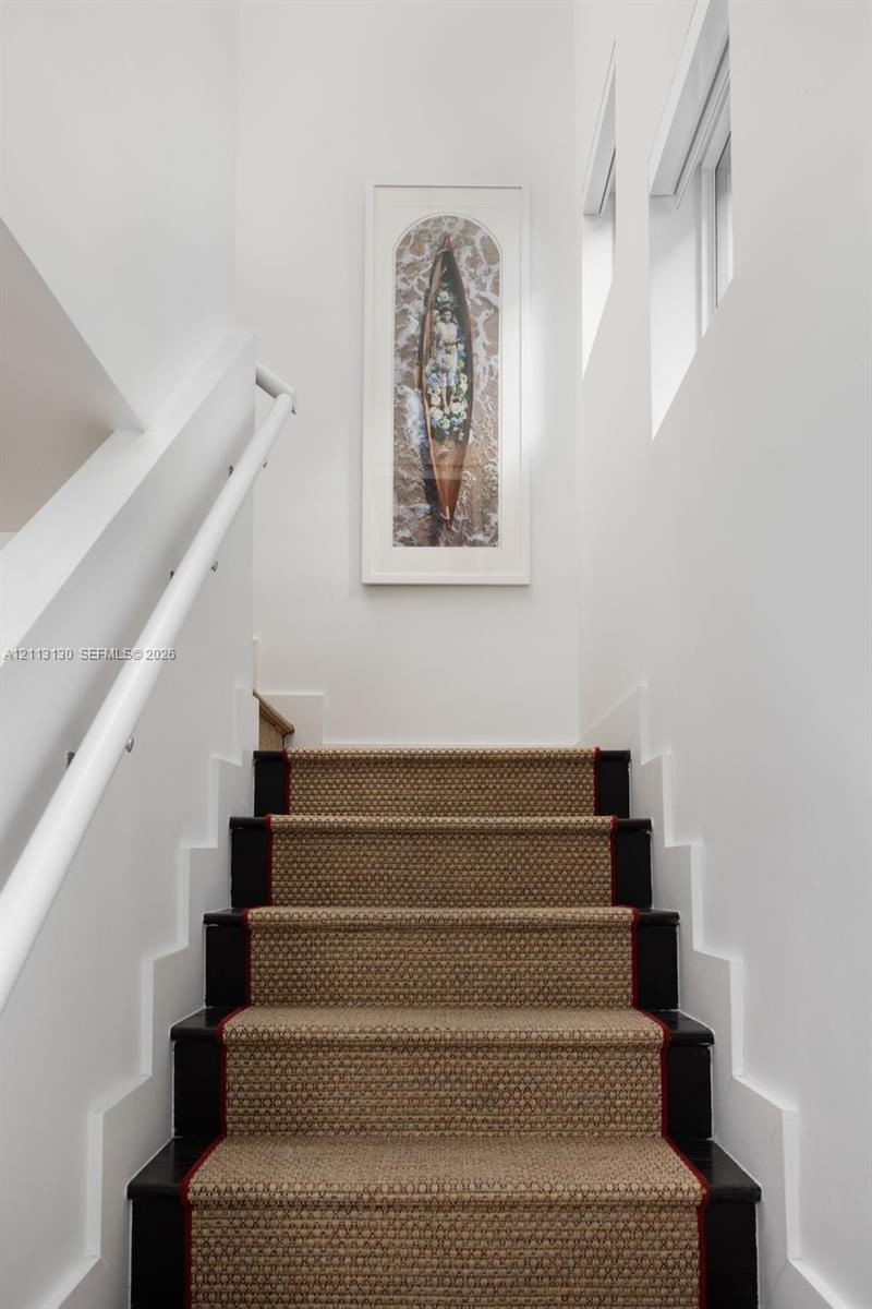 Staircase featuring dark-finished wooden treads, textured stair runner with a bordered edge, white wall-mounted handrail, and high-reaching walls with