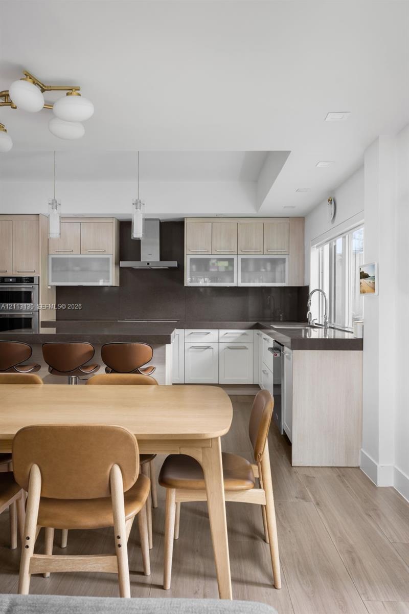 Kitchen featuring two-tone cabinetry with frosted-glass upper doors, dark solid-surface countertops, built-in stainless steel double wall oven, stainl