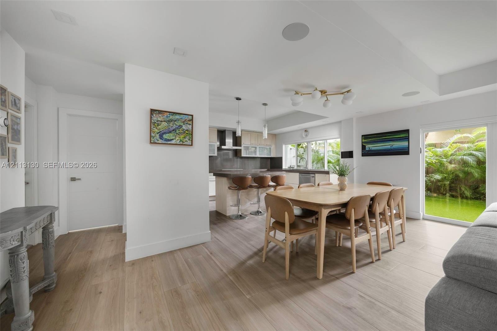 Open-concept interior featuring light wood-finish flooring, kitchen island with stone countertop, recessed ceiling speakers, modern multi-globe chande