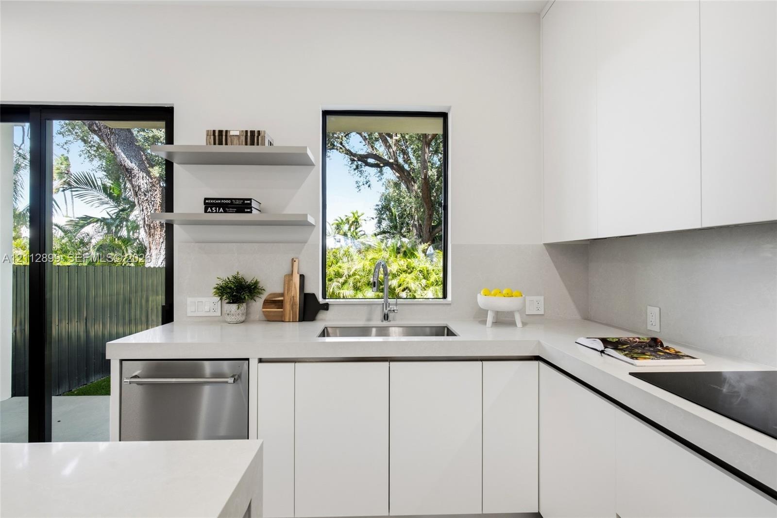 Minimalist kitchen featuring matte white flat-panel cabinetry, light-toned stone-surface countertops, stainless steel undermount sink, built-in dishwa