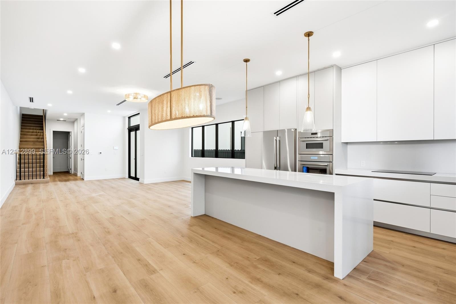 Modern kitchen featuring flat-panel cabinetry, a waterfall-edge quartz island, stainless steel built-in appliances, decorative pendant lighting, and w