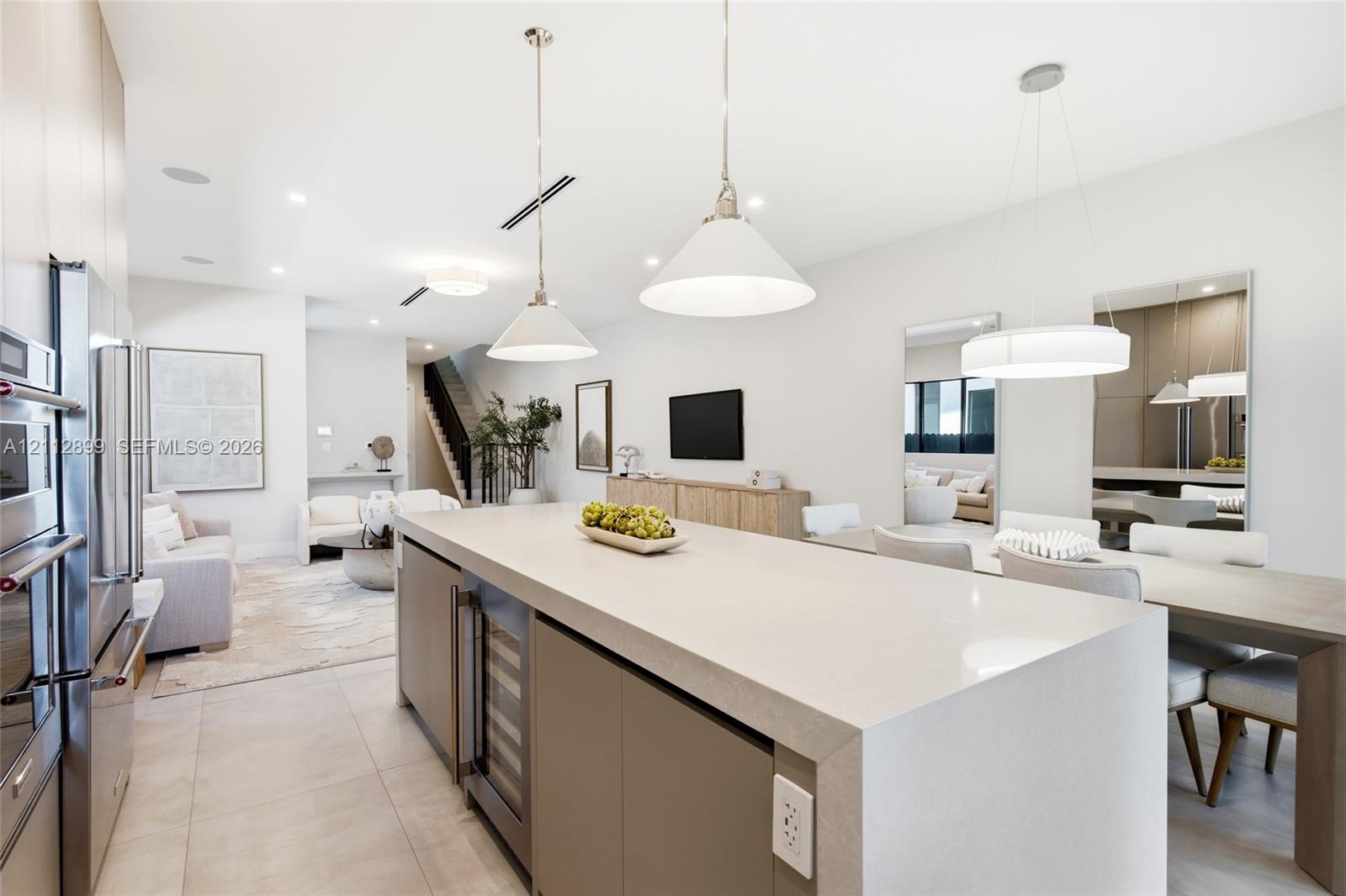 Large kitchen island with quartz waterfall countertop, integrated wine refrigerator, recessed lighting, matte-finish cabinetry, and oversized pendant 