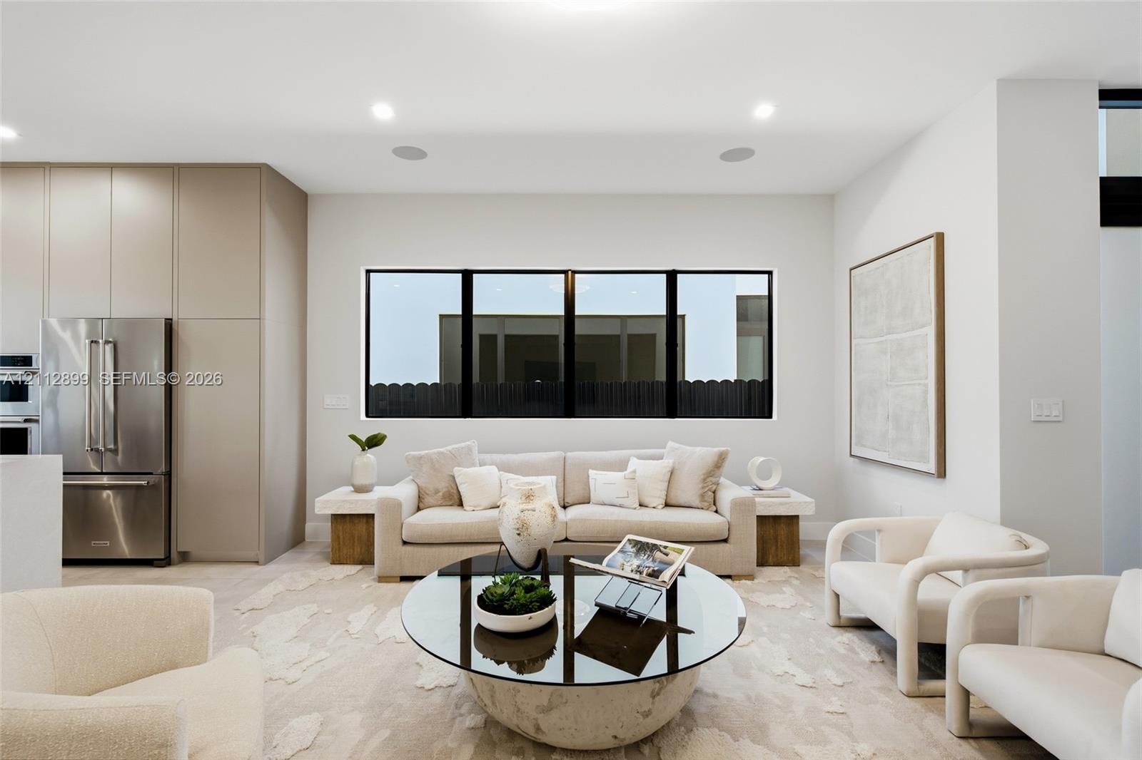 Open-concept living space featuring floor-to-ceiling cabinetry, stainless steel refrigerator, recessed lighting, and expansive tripartite black-framed