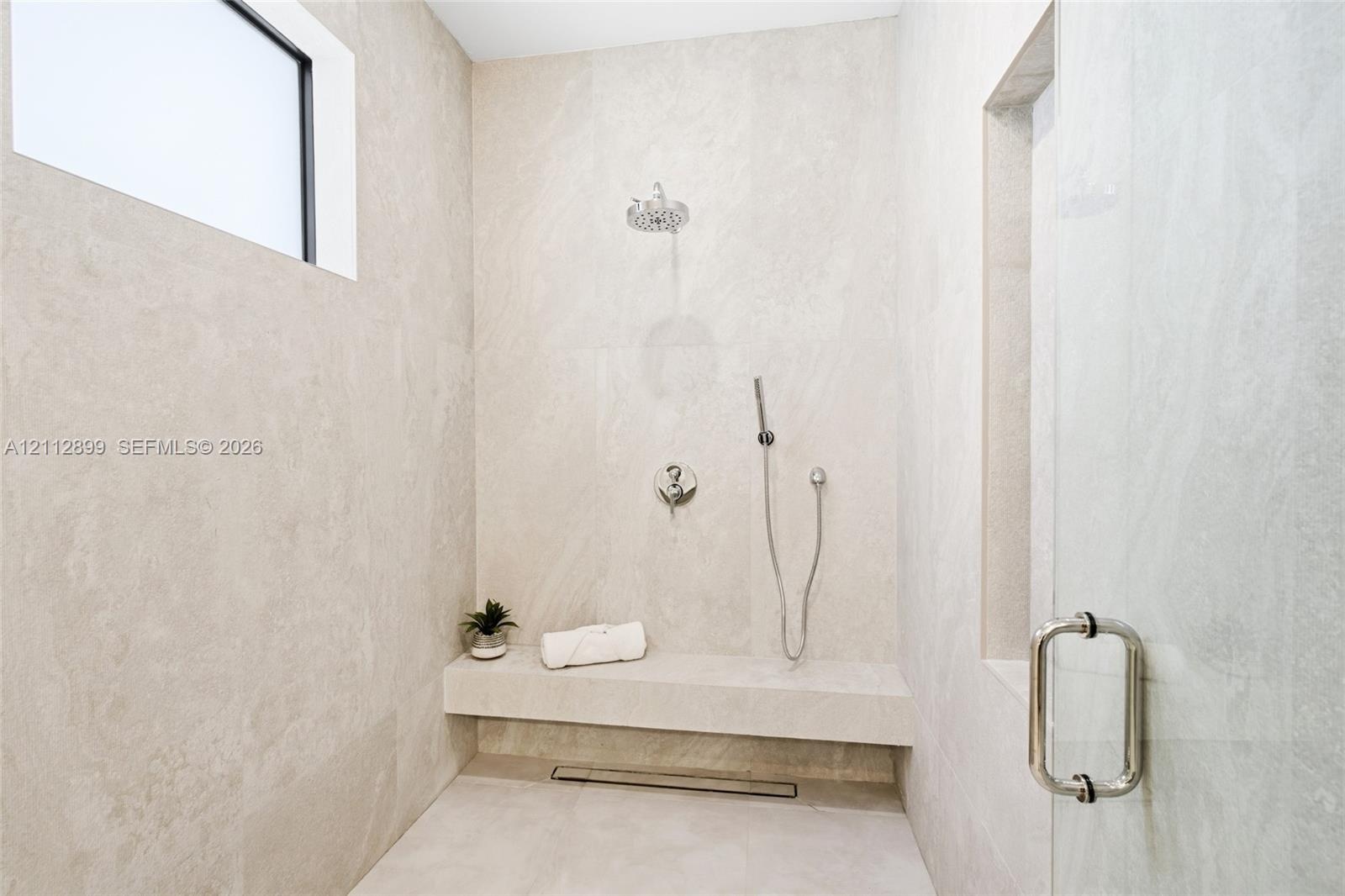 Walk-in shower featuring floor-to-ceiling stone-finish tile, a built-in stone bench, overhead rainfall showerhead, adjustable handheld shower wand, an