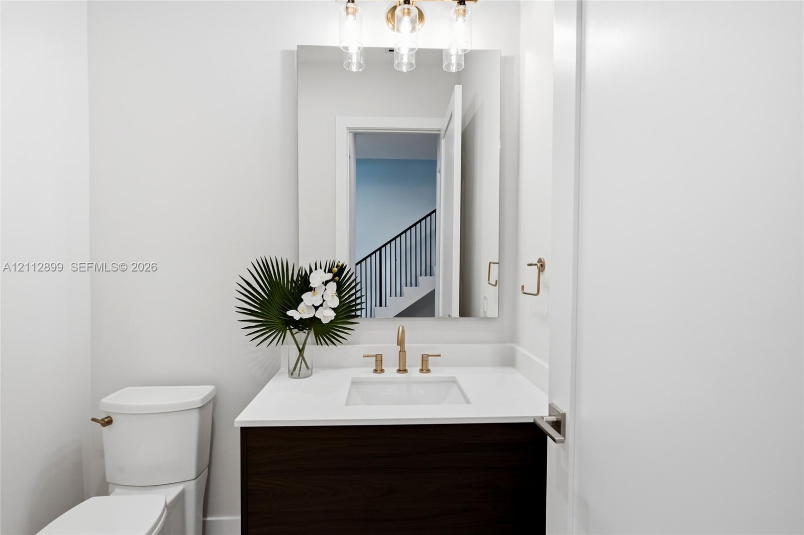 Bathroom featuring a dark wood-finish vanity, white countertop with an integrated basin, wall-mounted rectangular mirror, three-light fixture with cyl