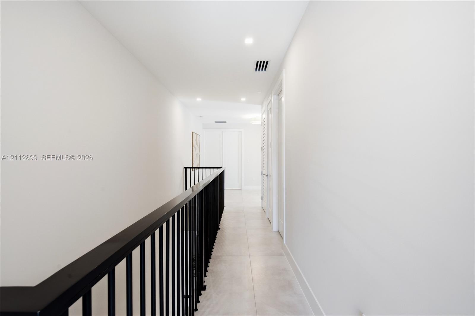 Hallway featuring large-format tile flooring, matte black metal railing, and recessed ceiling lighting