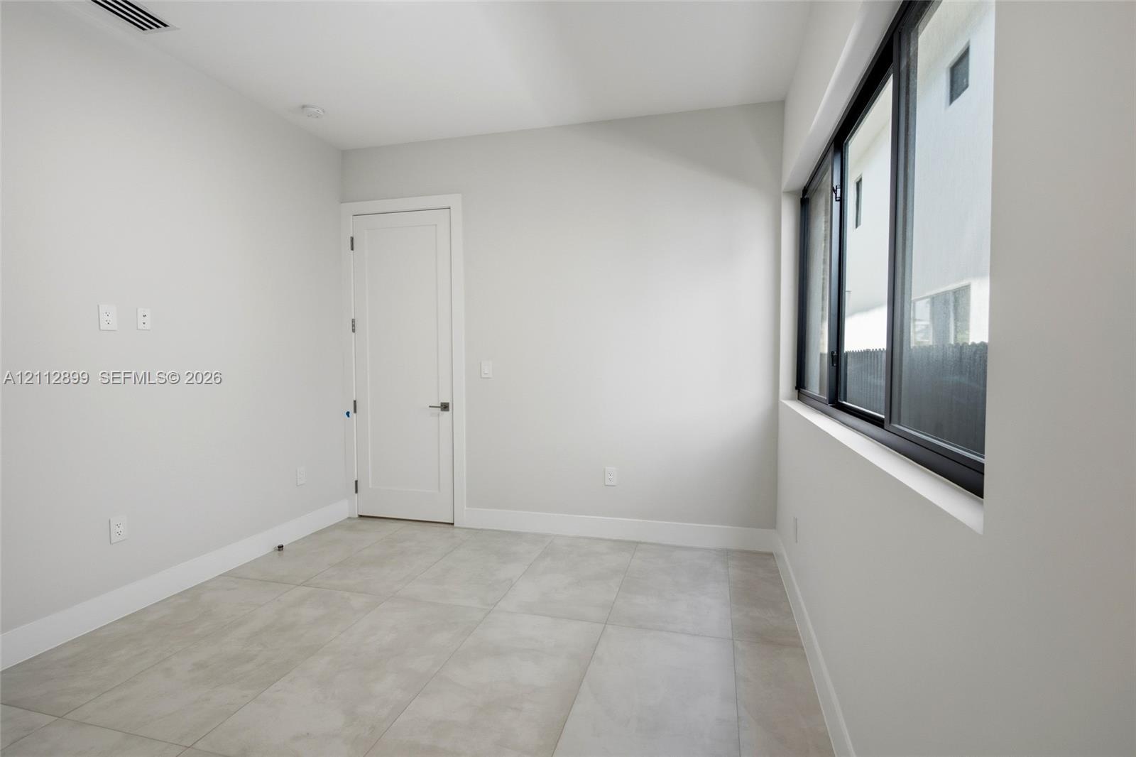 Room featuring large-format ceramic tile flooring, neutral wall paint, and a multi-pane window with dark frames