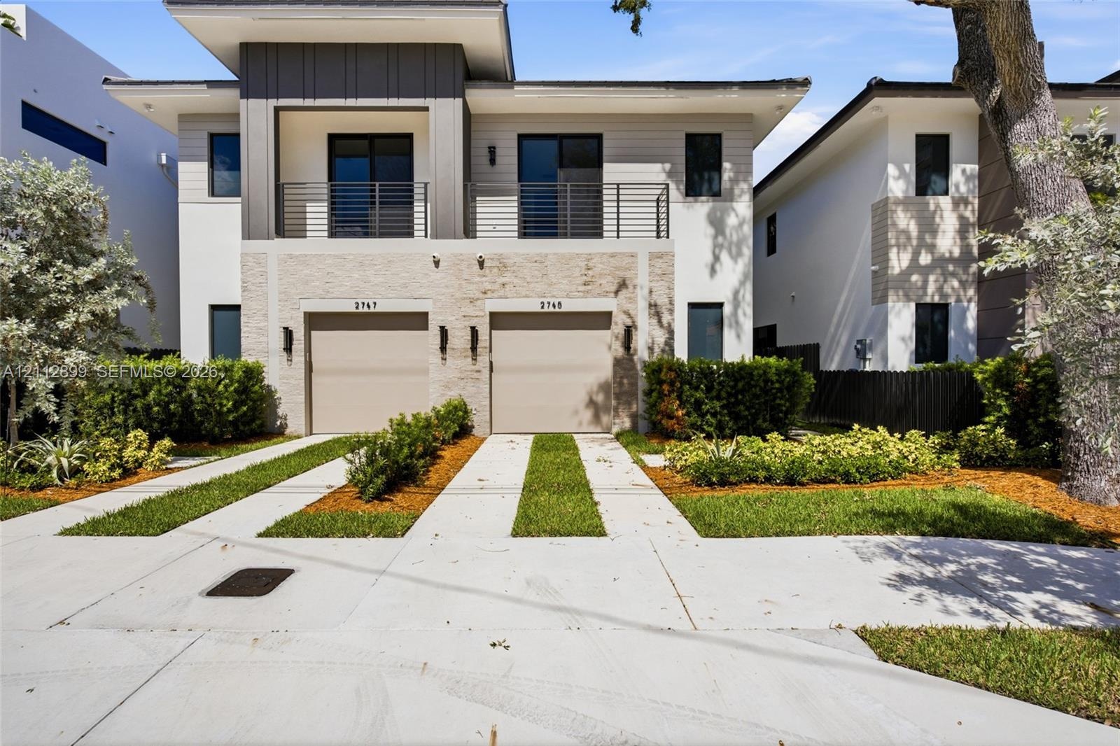 Modern exterior featuring a stacked stone facade, metal-accented second-story balcony with railings, dual two-car garage doors, and concrete paver dri