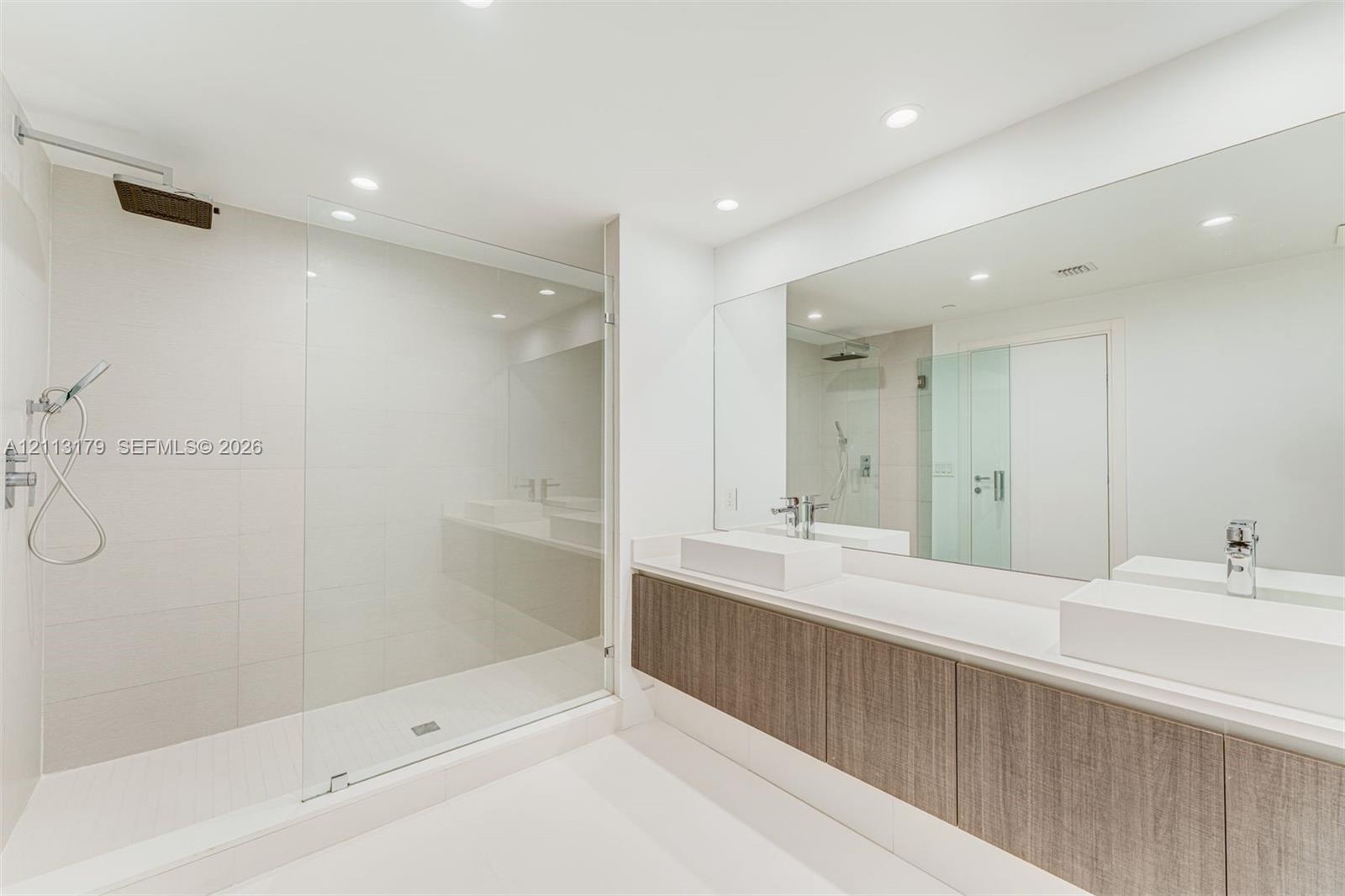 Dual vanity featuring rectangular vessel sinks, quartz countertops, wood-finish cabinetry, frameless glass shower enclosure, and ceiling-mounted rainf