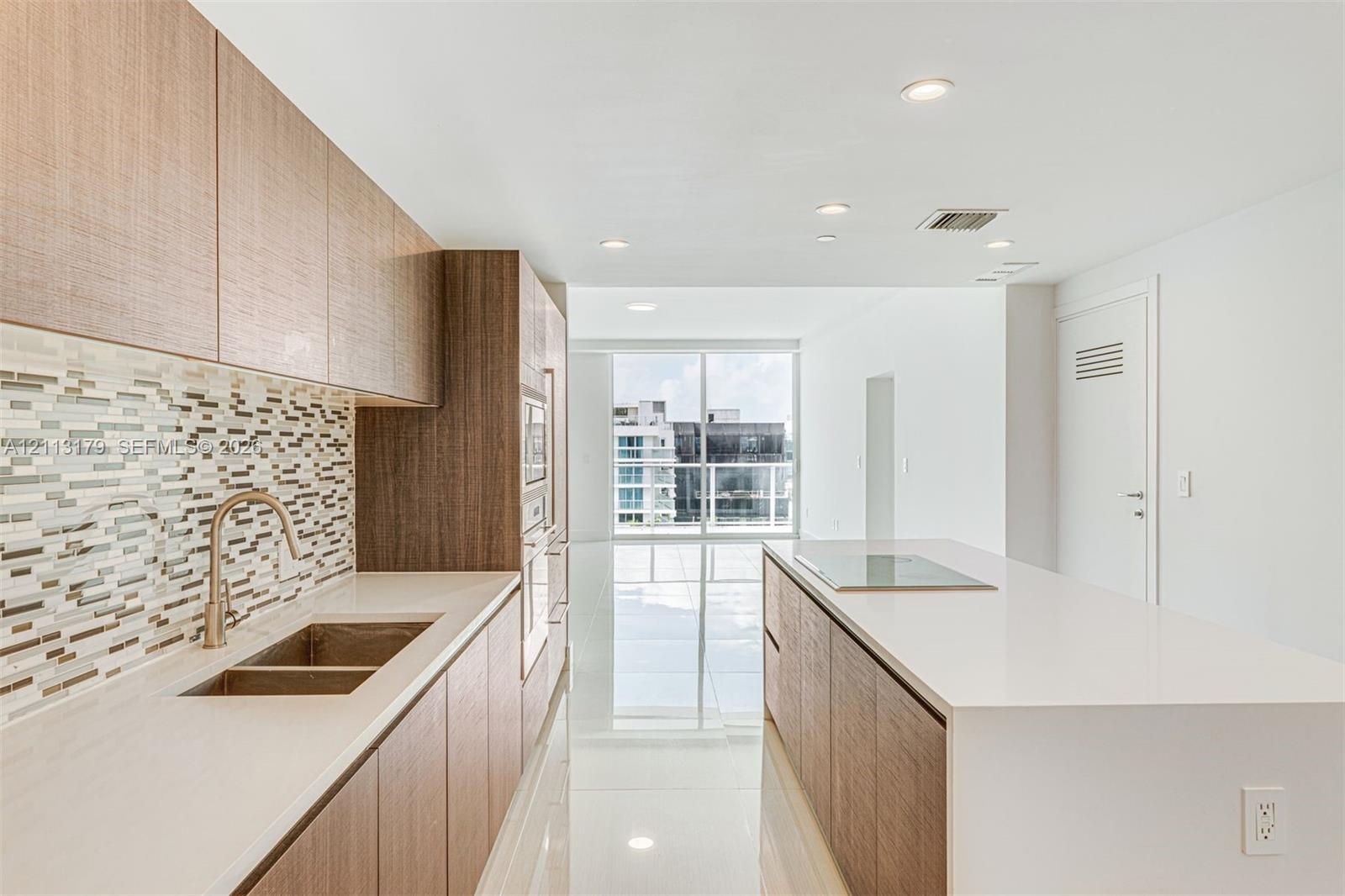 Kitchen featuring wood-finish cabinetry, stone-surface countertops, mosaic tile backsplash, integrated stainless steel appliances, and a central islan