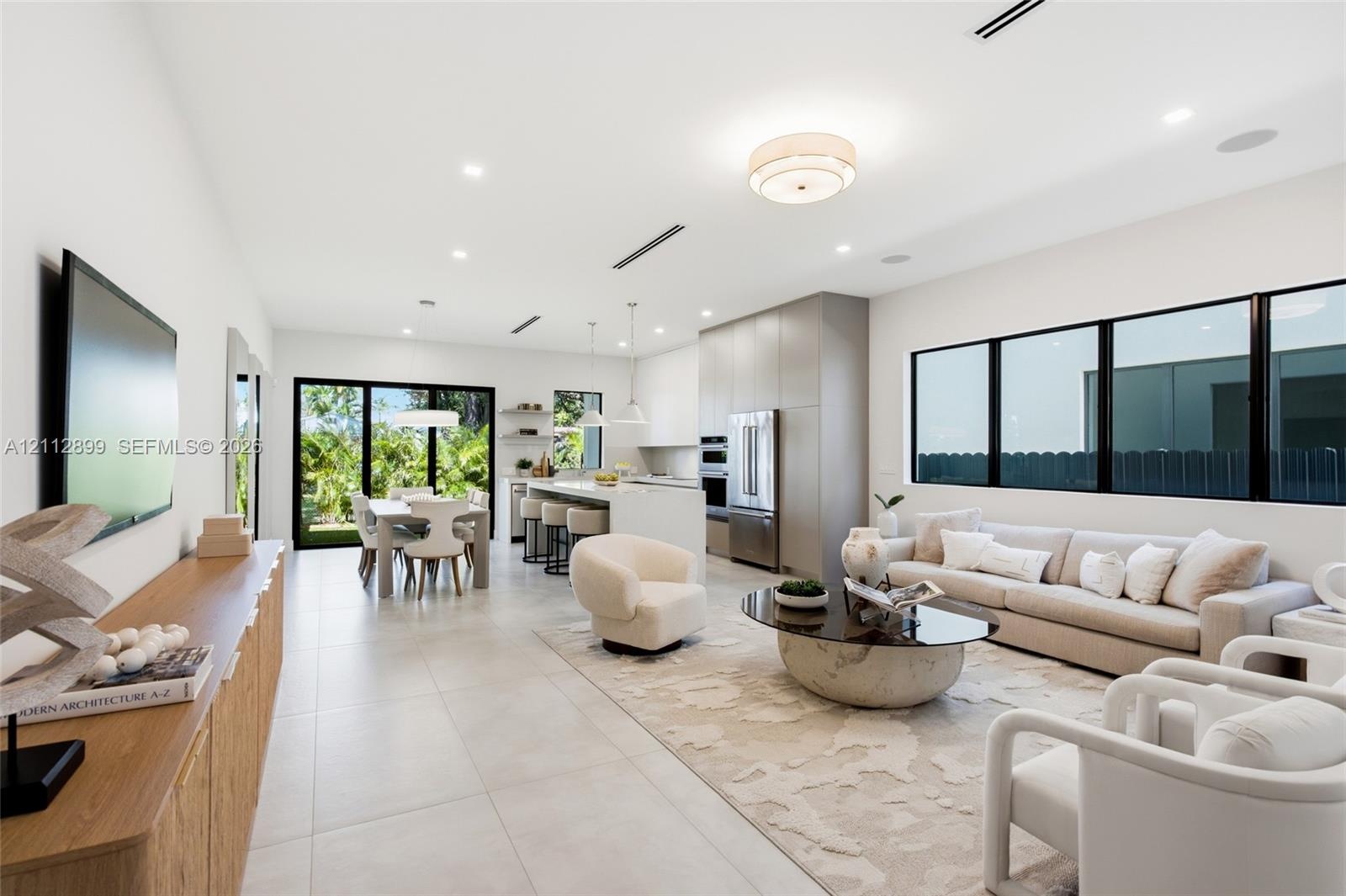 Open-concept interior featuring large-format tile flooring, recessed ceiling lighting, built-in kitchen cabinetry, stainless steel appliances, and bla