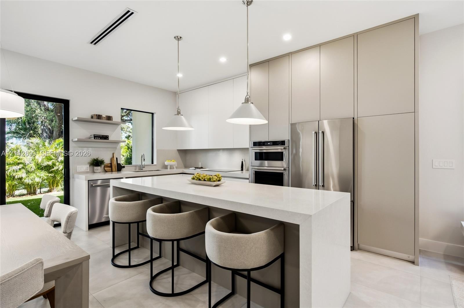 Contemporary kitchen featuring floor-to-ceiling flat-panel cabinetry, a waterfall-edge stone island, built-in stainless steel appliances, and dual pen