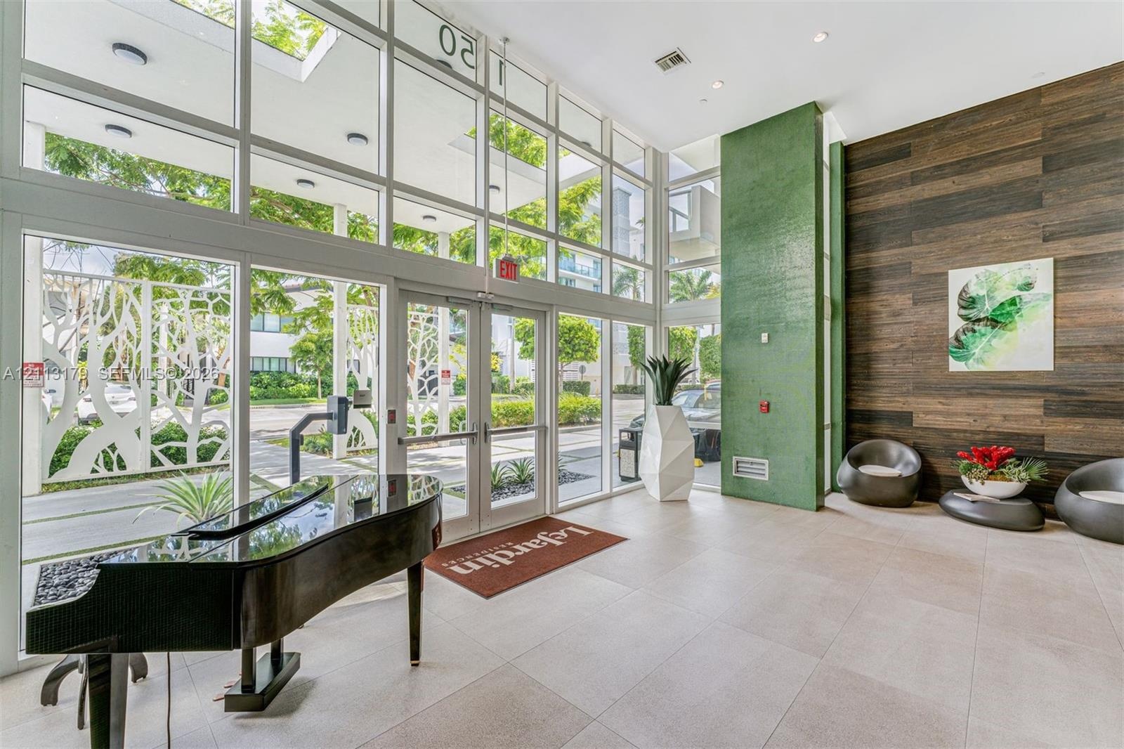 Grand entrance lobby featuring double-height glass curtain walls, floor-to-ceiling windows, large-format tile flooring, a vibrant green accent pillar,