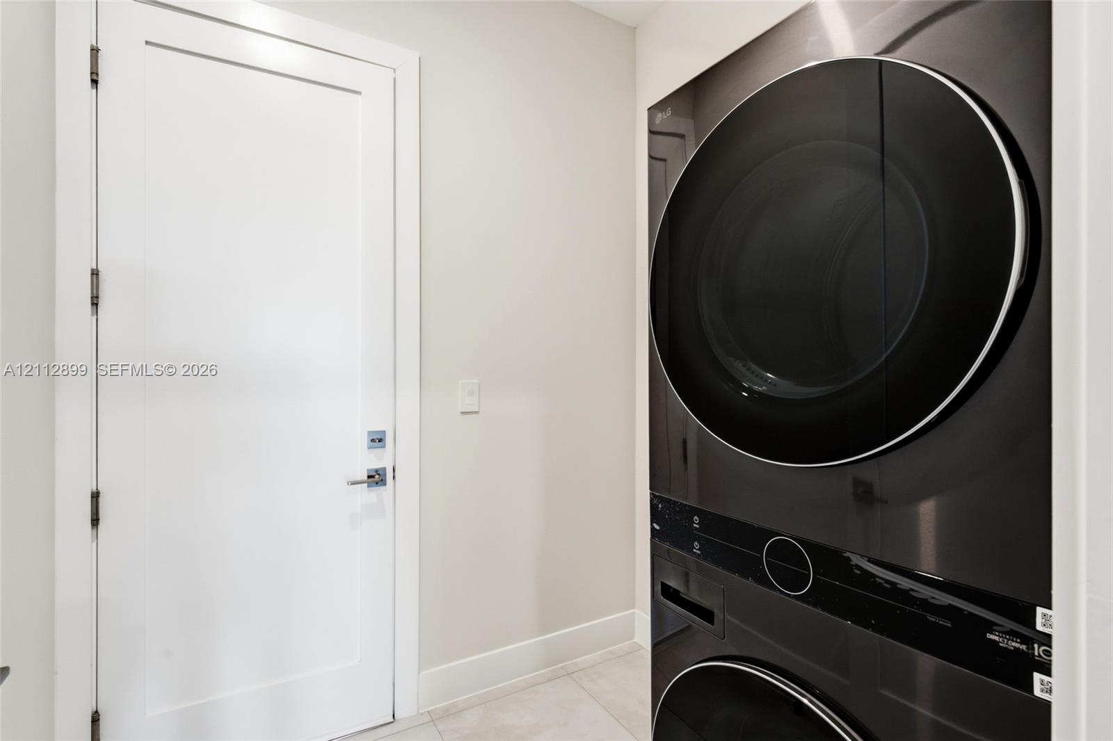 Stacked washer and dryer unit with a sleek black finish, paired with a white Shaker-style door featuring polished chrome hardware and large-format til