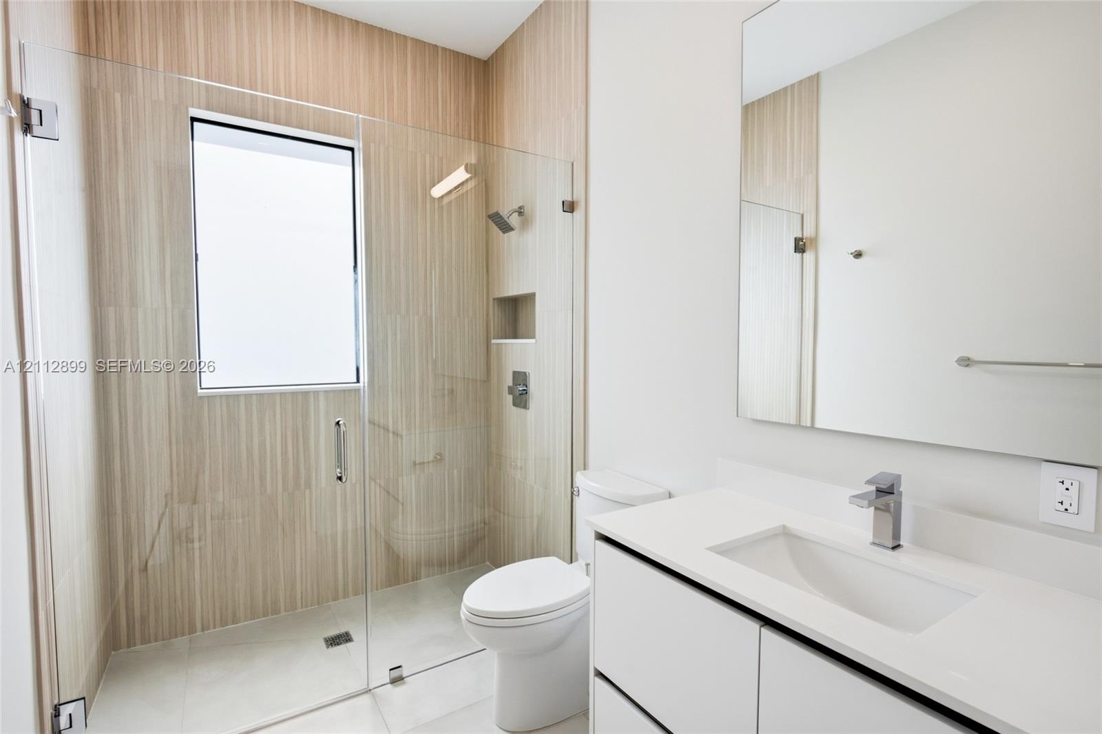 Modern bathroom featuring a glass-enclosed shower with vertical-tile surround, built-in recessed wall niche, wall-to-wall mirror, and white vanity wit