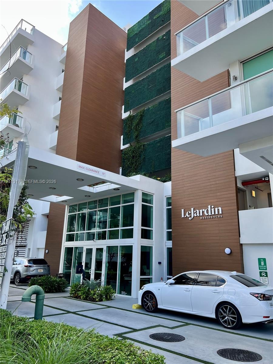 Modern building facade featuring wood-finish paneling, vertical green wall detailing, expansive floor-to-ceiling glass entryway, white structural acce