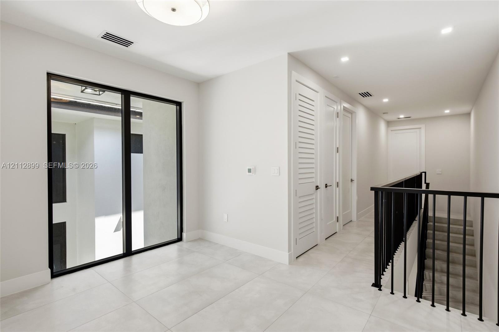 Large-format tile flooring, black-framed floor-to-ceiling glass window, recessed lighting, and a staircase with a black metal railing