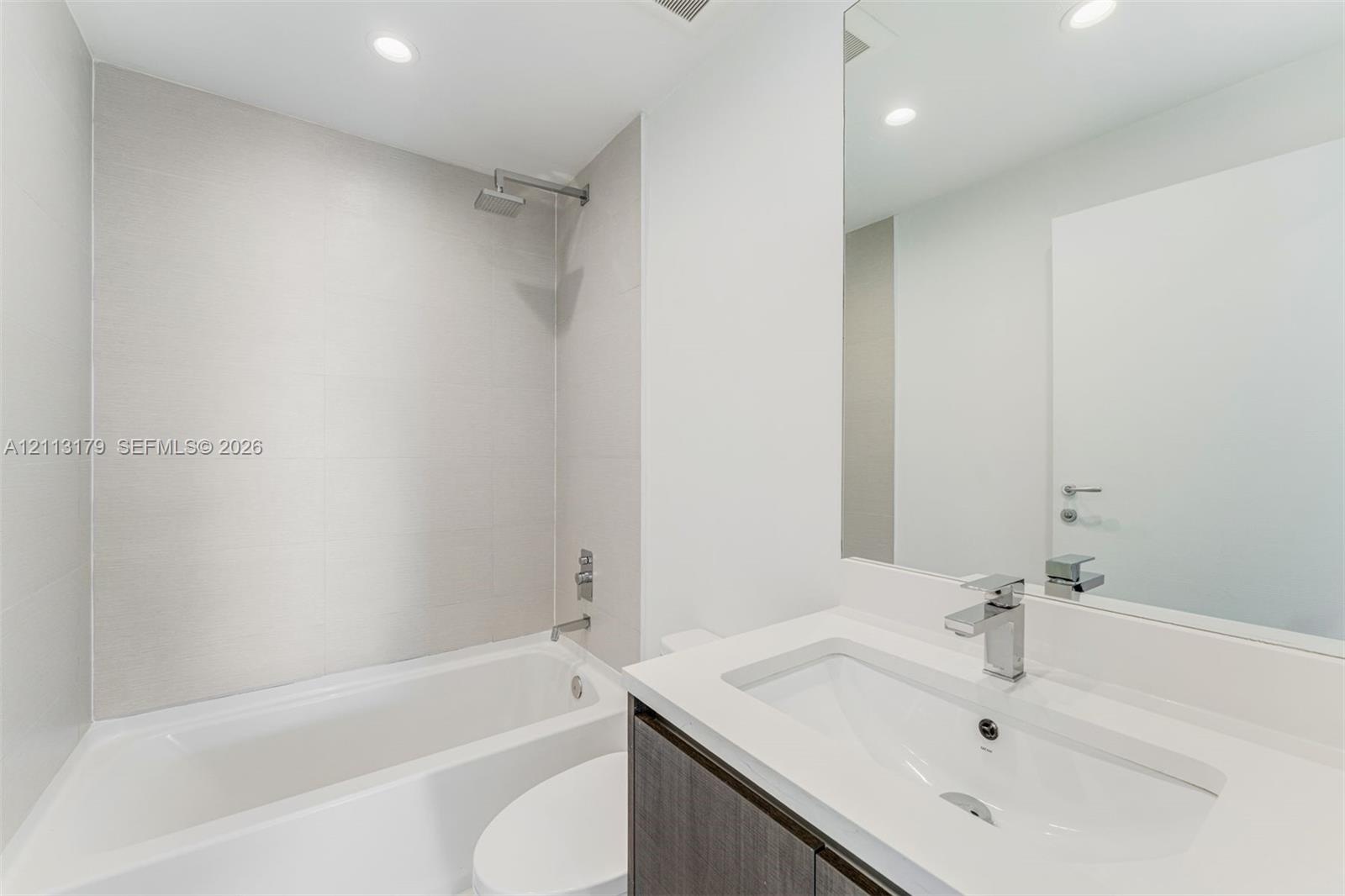 Bathroom featuring a large-format tiled shower surround with a rain-style showerhead, a deep soaking tub, and a vanity topped with a rectangular integ