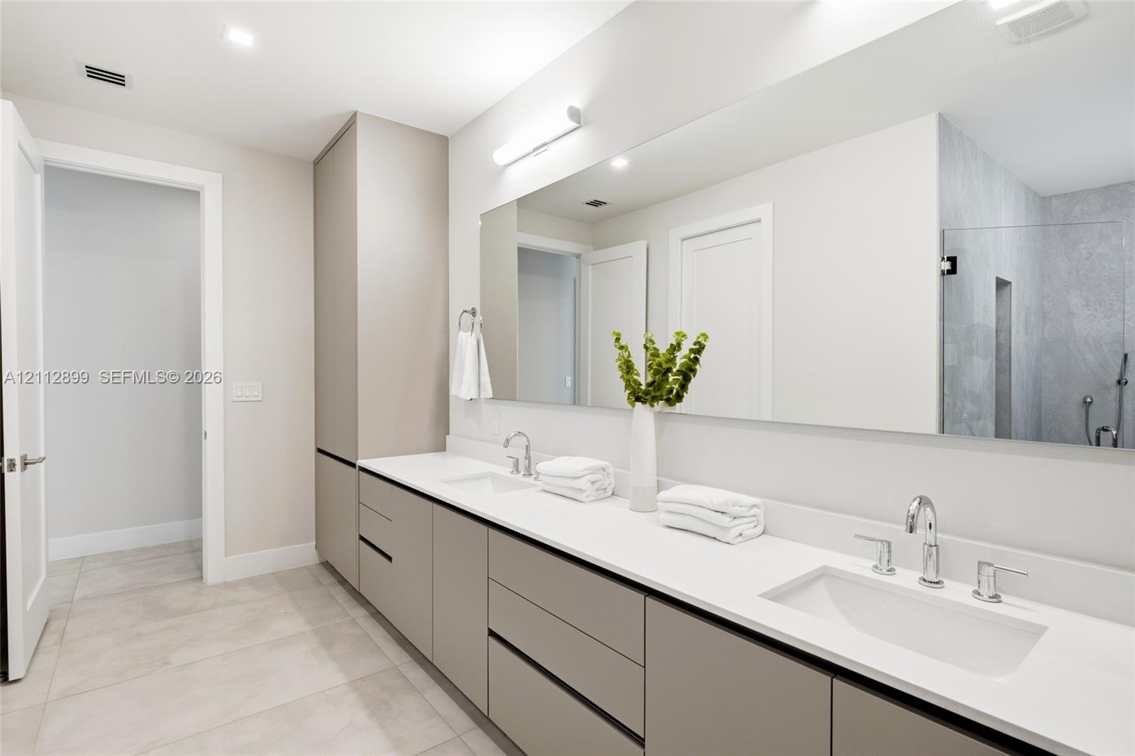 Extended vanity featuring flat-panel cabinetry, light-toned solid surface countertops, dual undermount sinks, and a large-format vanity mirror with in