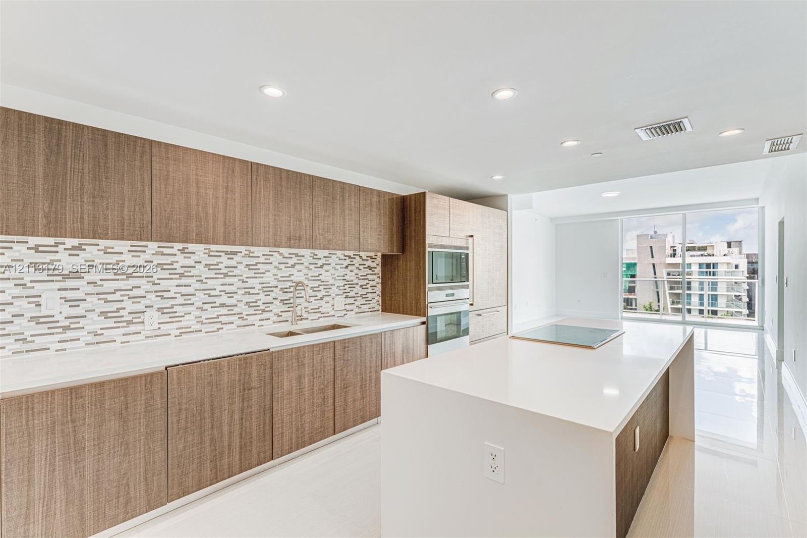 Kitchen featuring wood-finish cabinetry, quartz countertops, mosaic tile backsplash, built-in wall oven and microwave, and a large center island with 