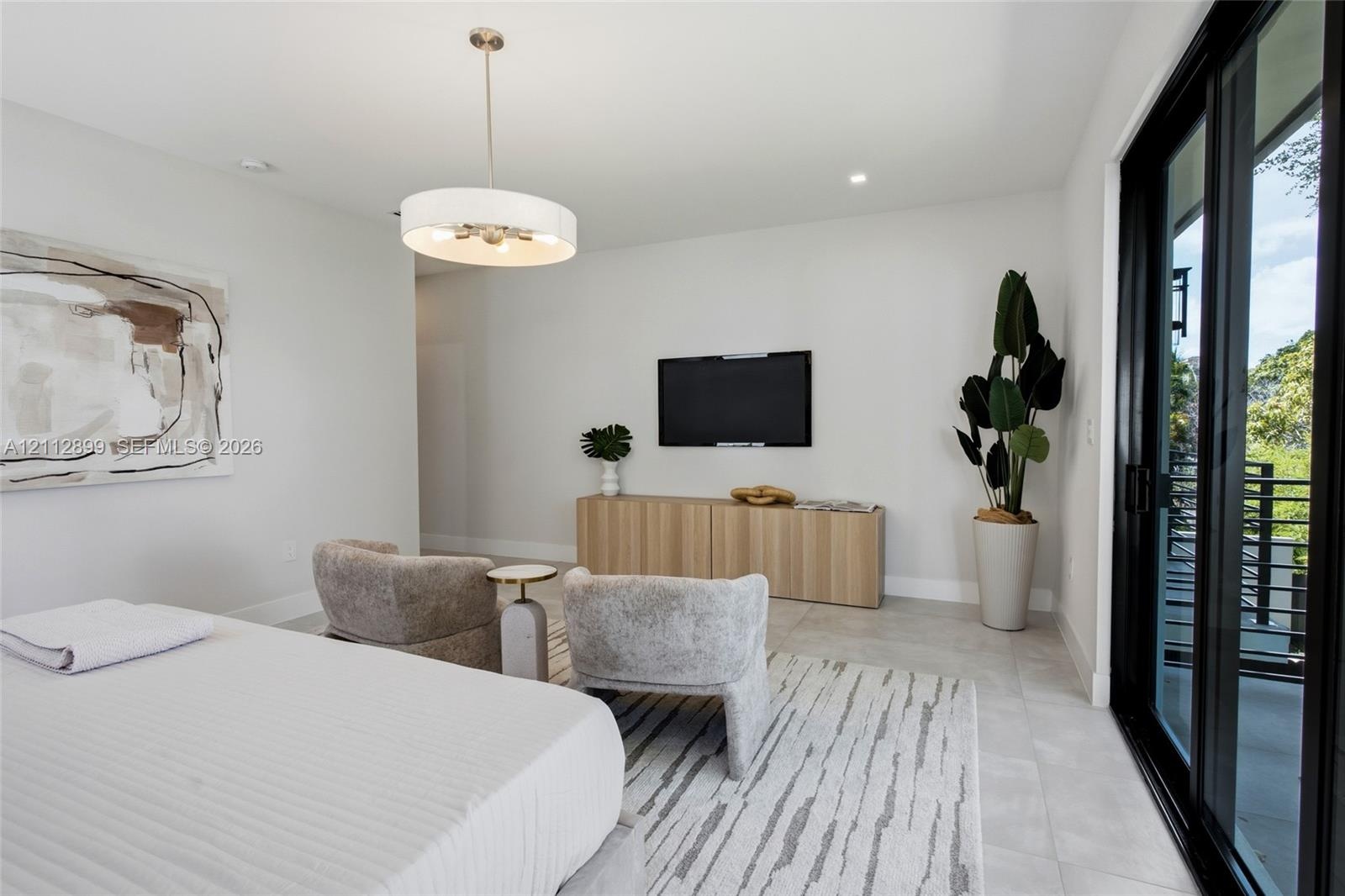 Neutral-toned interior featuring large-format tile flooring, a contemporary drum pendant light fixture, and black-framed sliding glass doors opening t