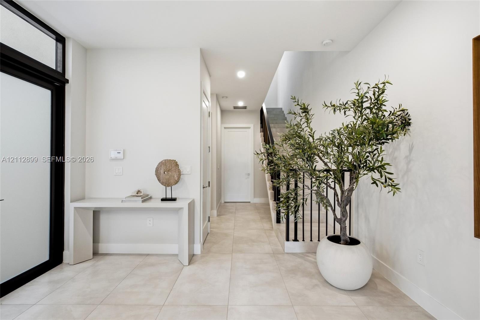 Entryway featuring large-format tile flooring, a glass-paneled front door with black trim, recessed lighting, and a staircase with black metal baluste