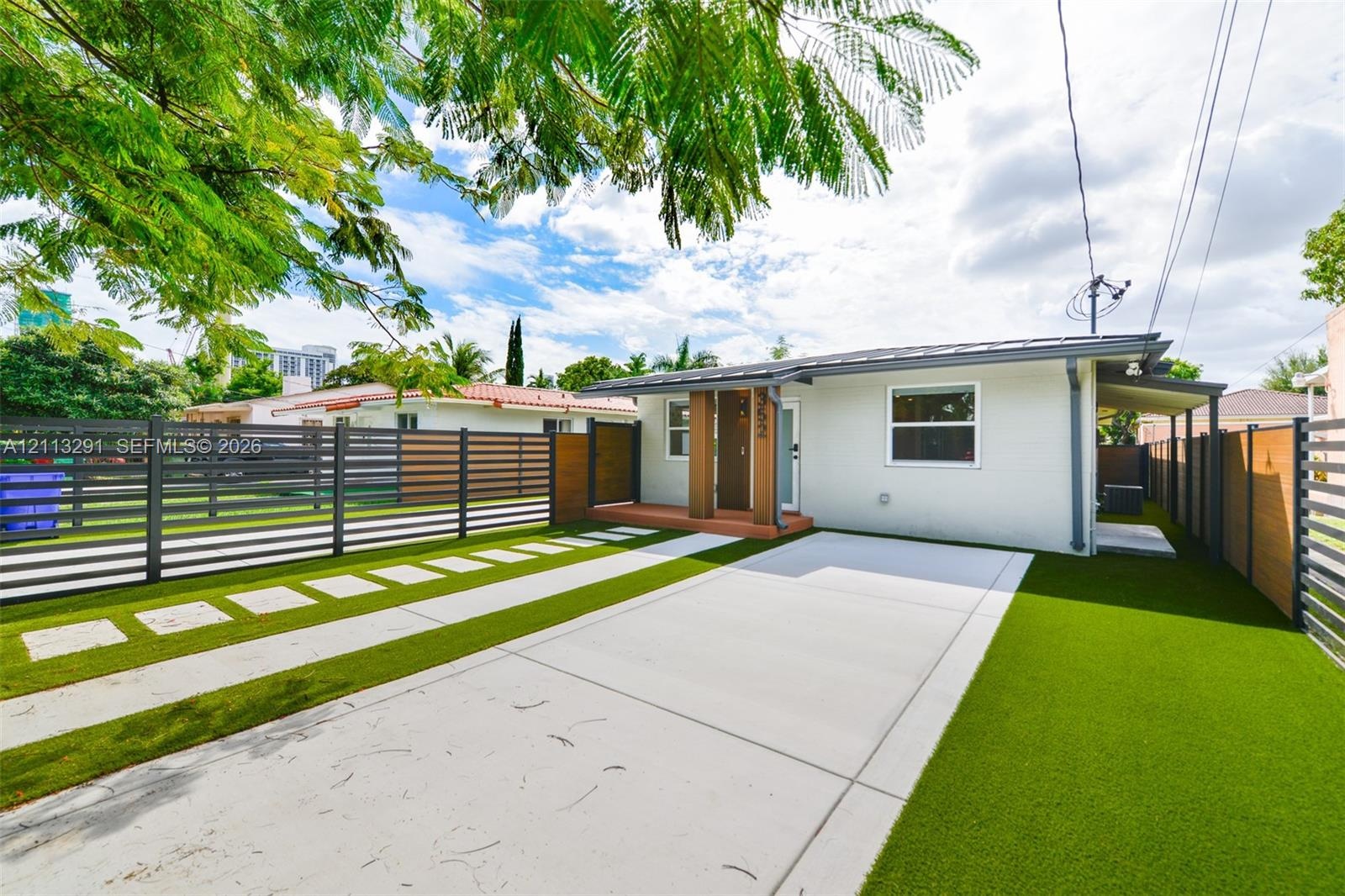 Exterior featuring light-colored masonry, horizontal slat fencing, a concrete driveway, paver stepping stones, and synthetic turf lawn