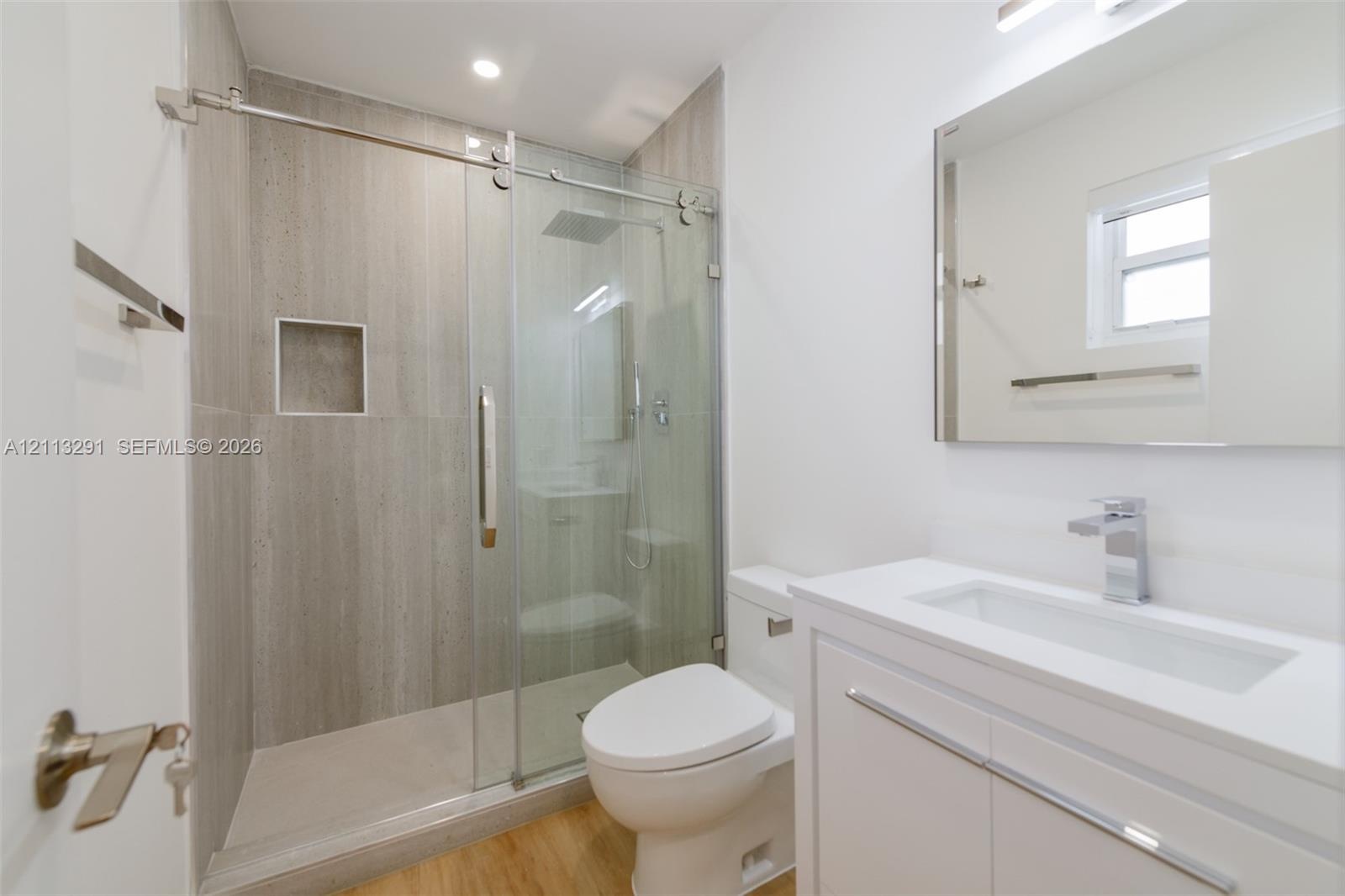 Bathroom featuring a glass-enclosed shower with floor-to-ceiling tile, built-in recessed niche, modern vanity with a white countertop, and wood-finish