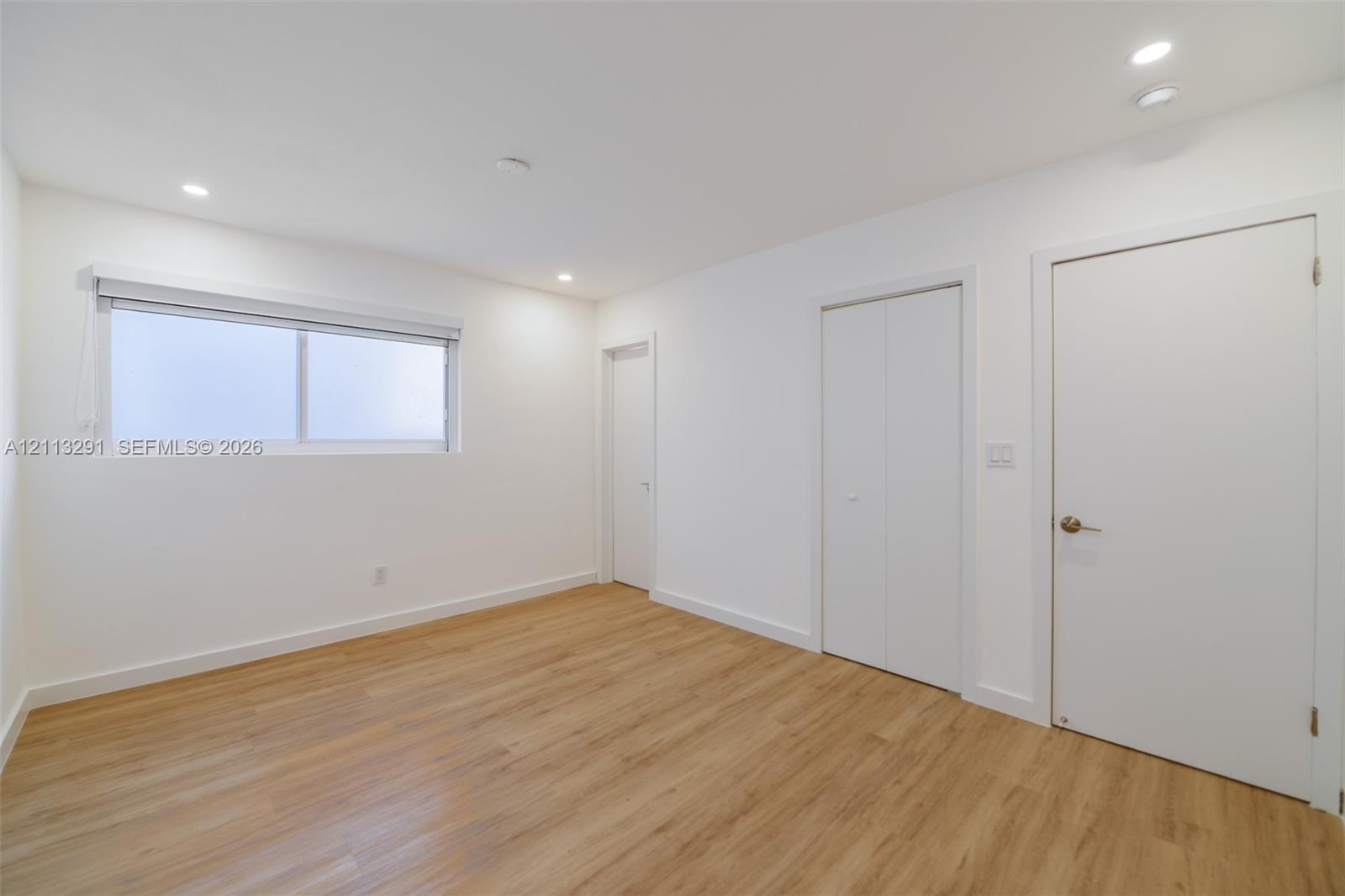 Neutral-toned interior featuring wood-finish flooring, recessed lighting, a horizontal sliding window, and solid-core doors