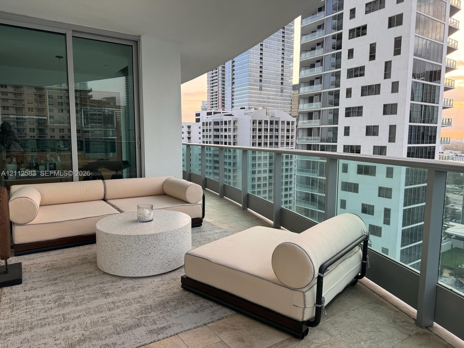 Covered balcony featuring natural stone tile flooring, glass-panel railings, and floor-to-ceiling sliding glass doors