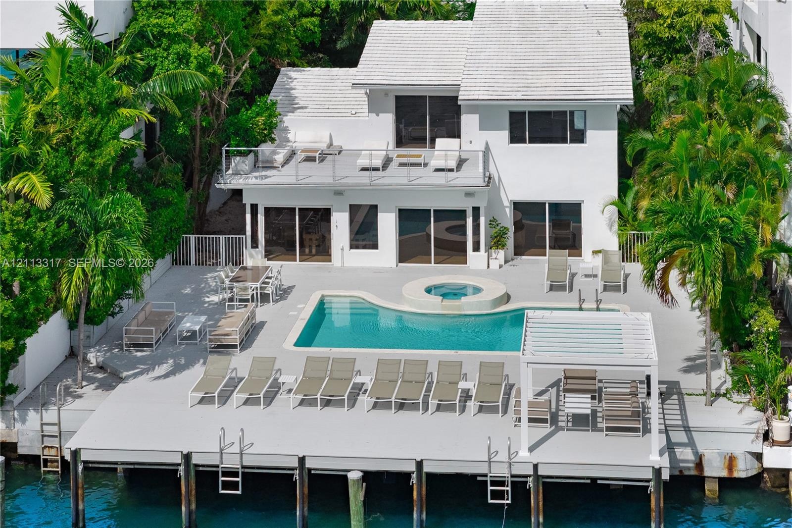 Two-story exterior with white siding and a tiled roof, featuring an expansive waterside deck, a swimming pool with an integrated spa, and a private do