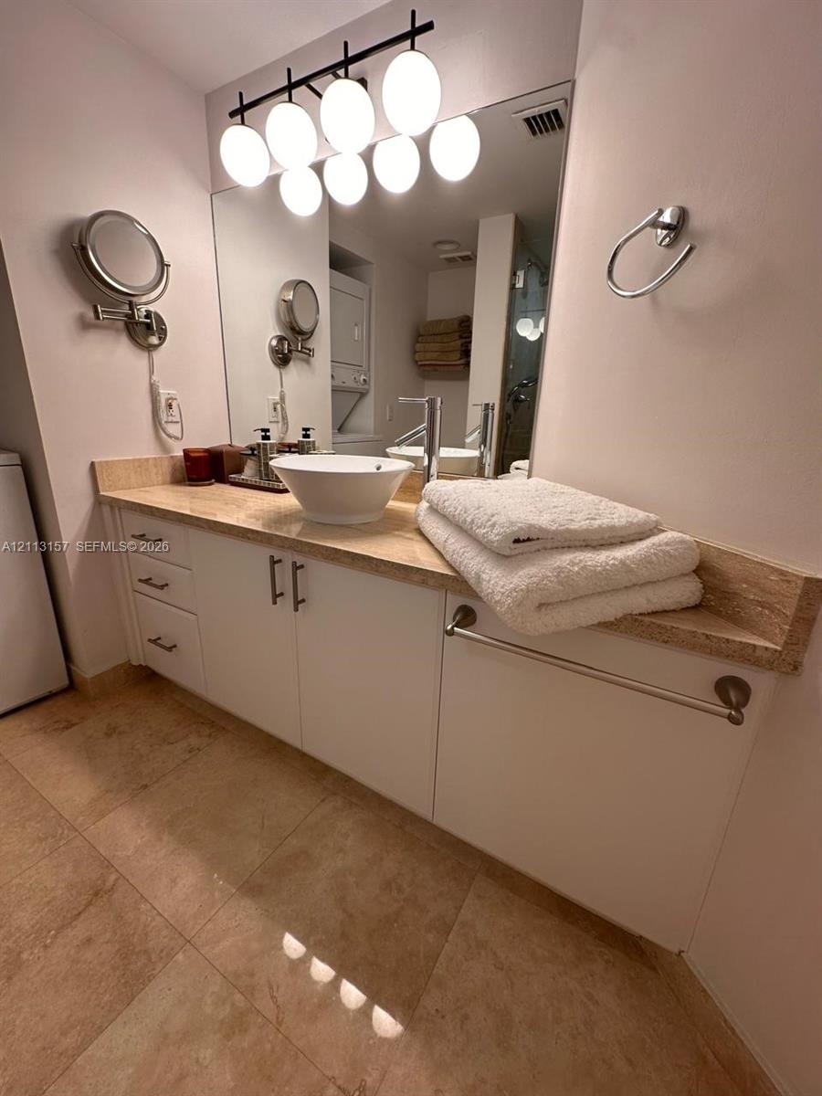 Vanity featuring a vessel sink, stone countertop, white cabinetry with metal hardware, large wall-mounted mirror, and multi-bulb overhead lighting