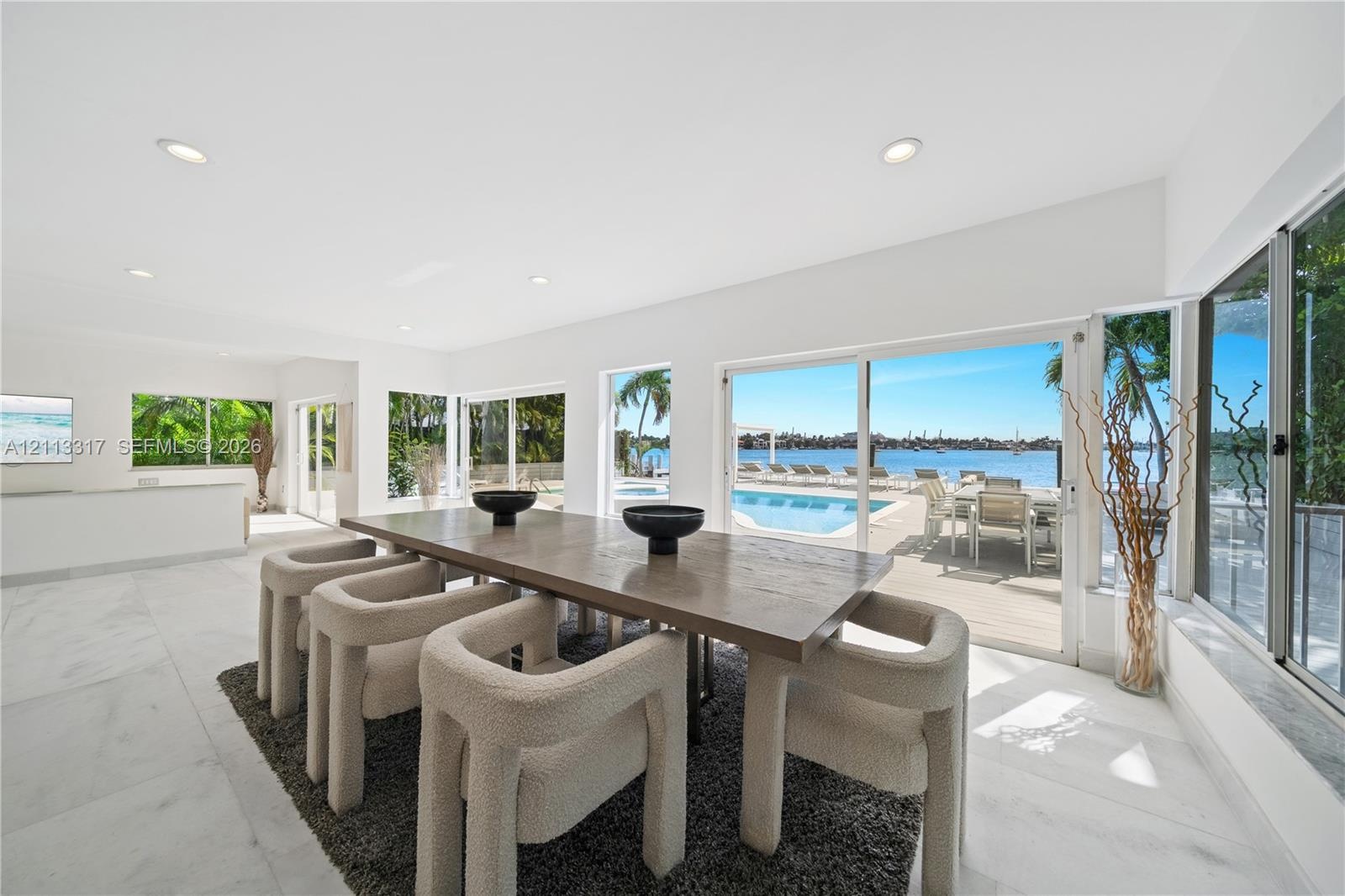 Open-concept interior featuring large-format tile flooring, recessed lighting, and expansive floor-to-ceiling glass sliding doors opening to an outdoo