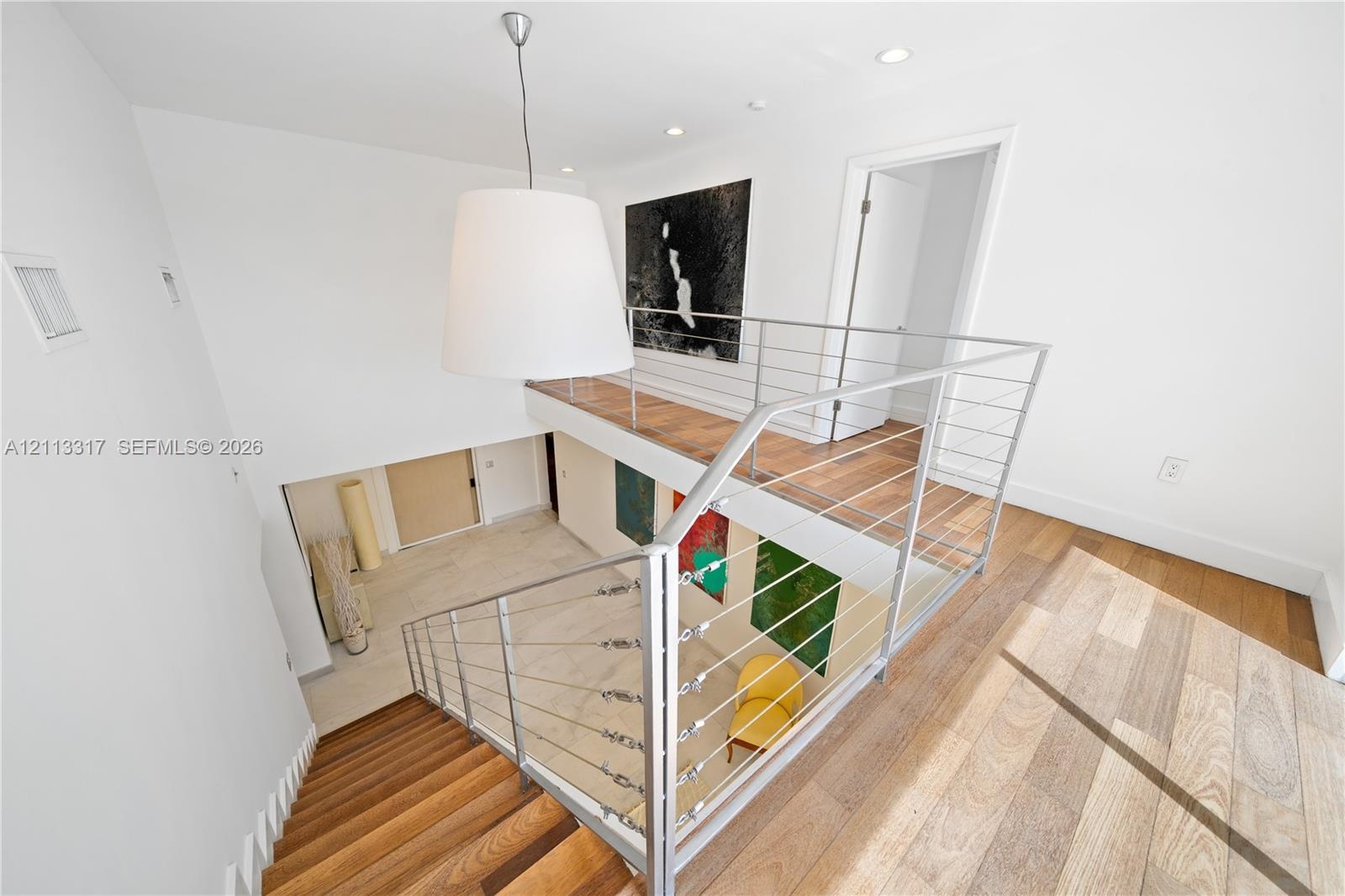Staircase featuring wood-finish treads, metal cable railing system, recessed lighting, and a large drum pendant light