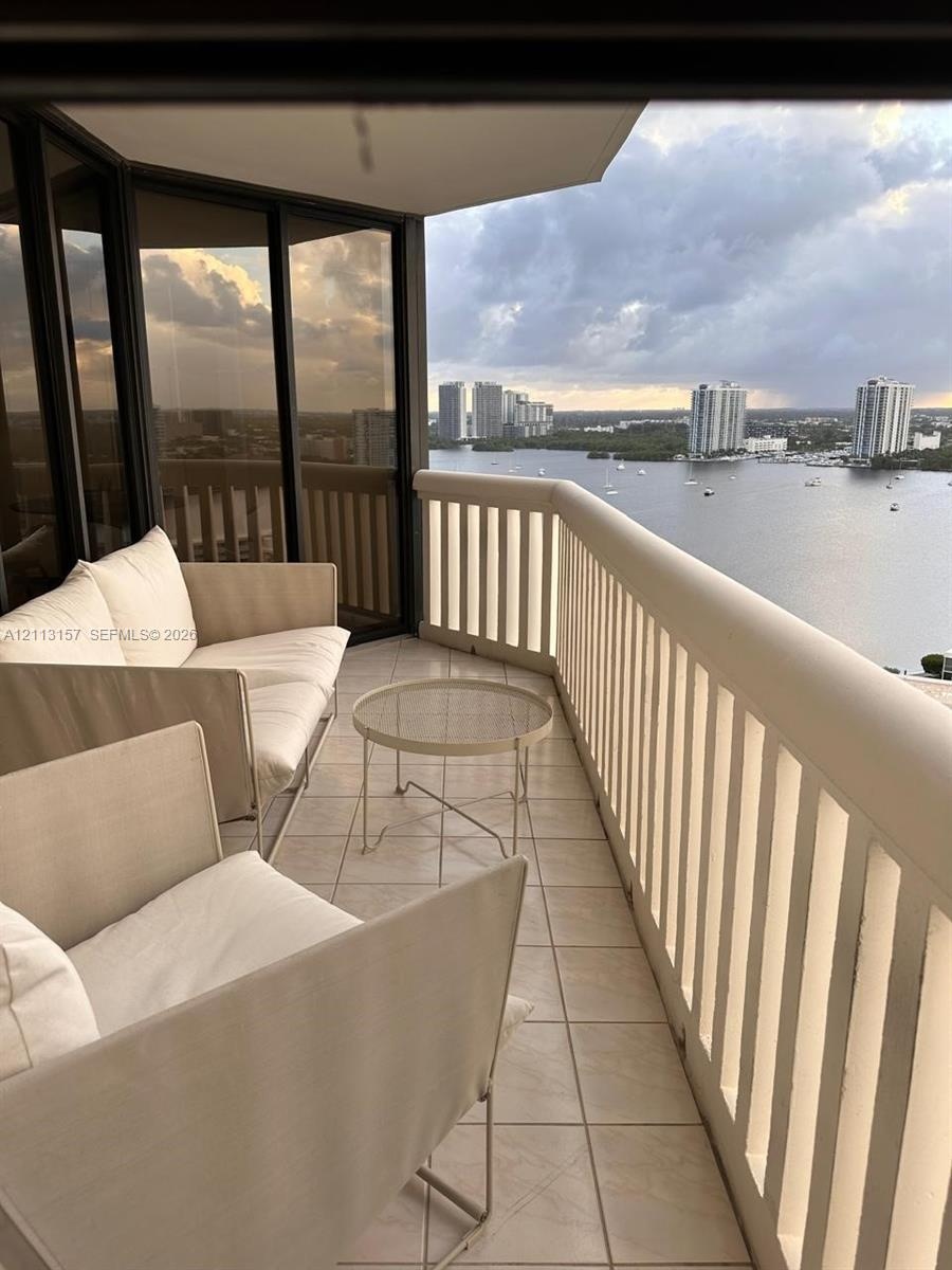 Private balcony featuring tiled flooring, a floor-to-ceiling glass enclosure, and a high-profile structural railing overlooking the water and city sky