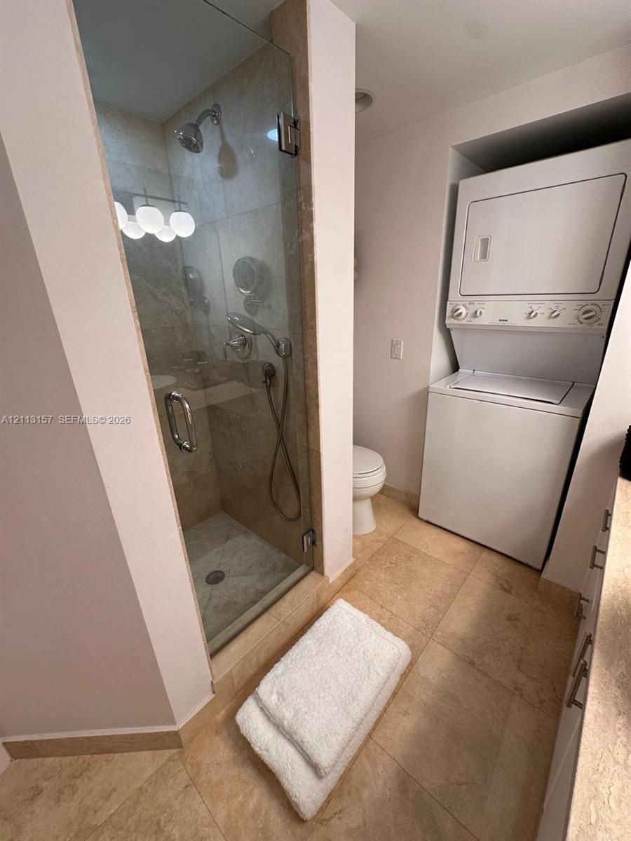 Walk-in shower with a glass door, stone-finish wall tiling, integrated stacked laundry unit, and stone-finish floor tiling